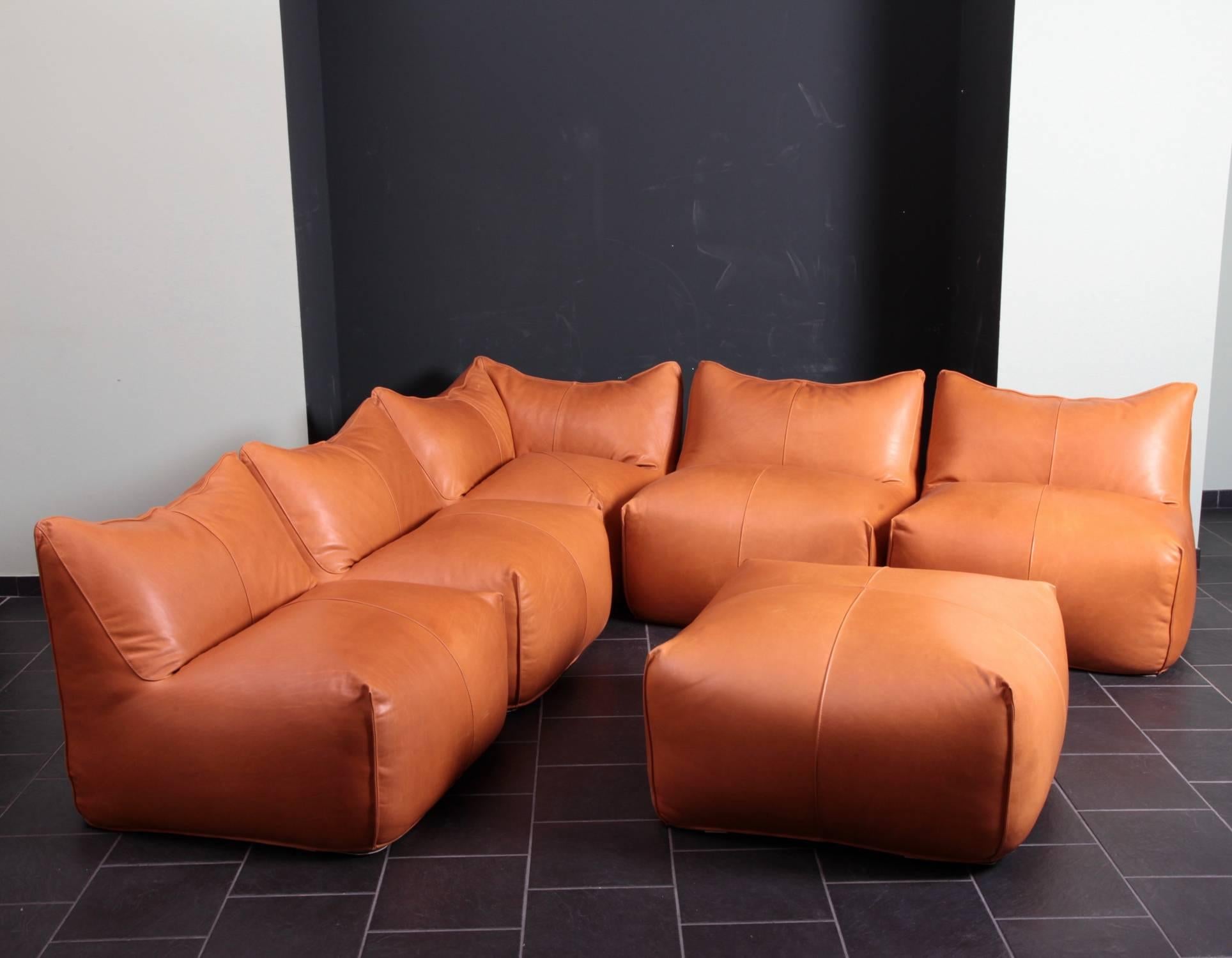 New upholstered set with one corner piece, four lounge chairs and one ottoman pouf. The set is upholstered in a high quality aniline tan leather. We had to replace some of the bottom fabrics due to condition. It is also possible to connect the pcs