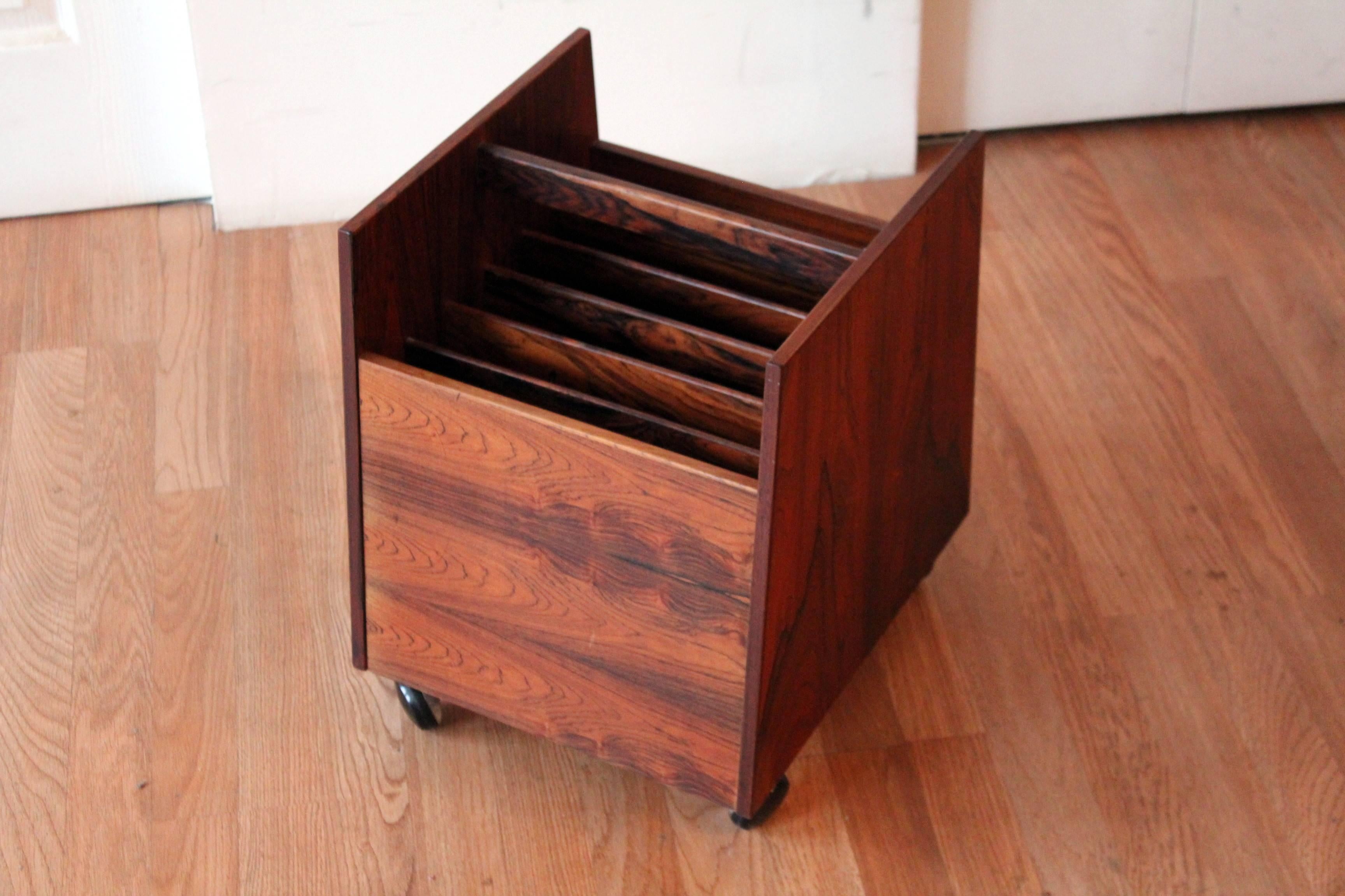 This rosewood magazine rack by Brusko, made in Norway, does double duty as a magazine rack or record storage cabinet. The piece, which features six storage compartments, rests on four smooth rolling casters and is beautifully labeled showing its