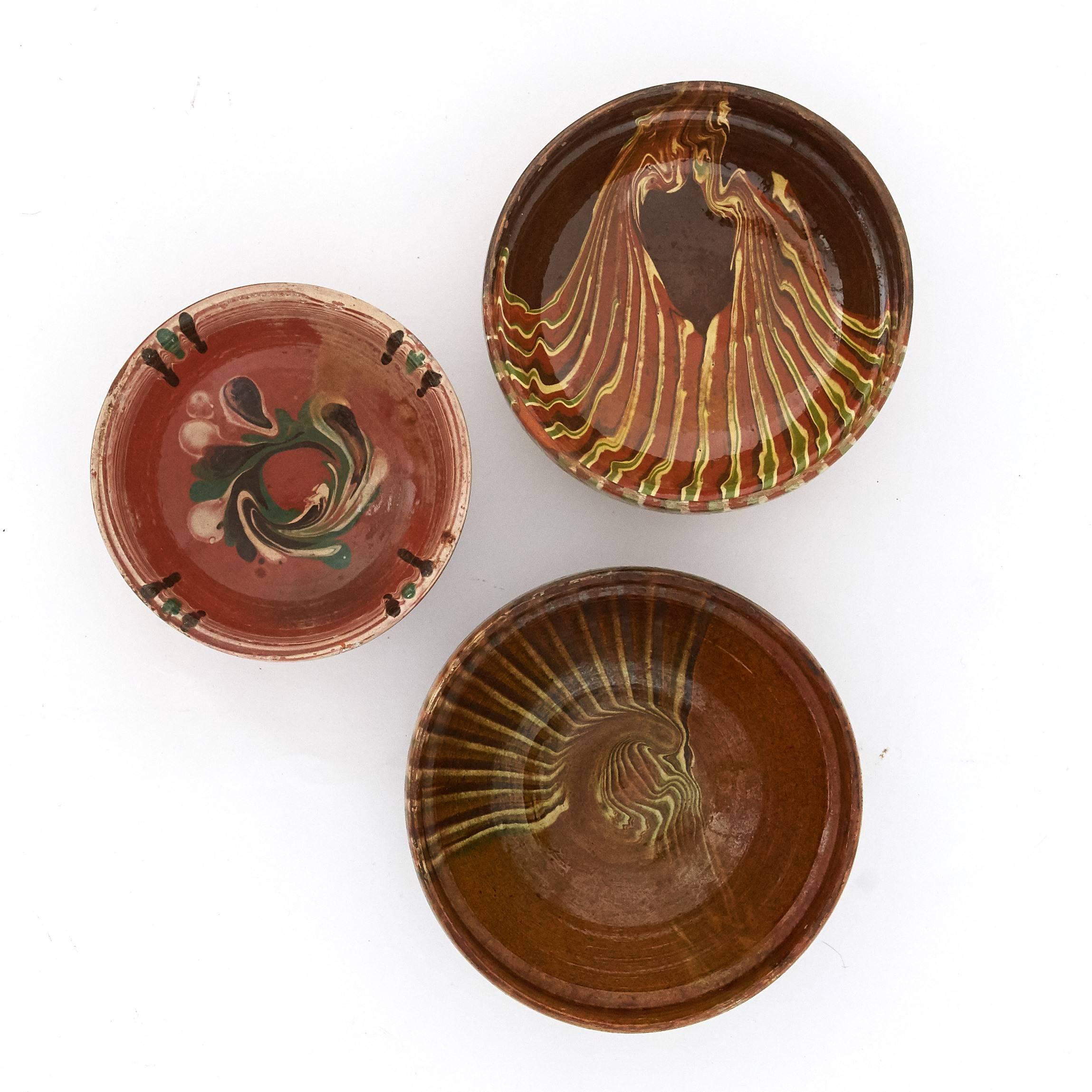 All three bowls were crafted in Romania in the mid-20th century. They are made in terracotta and then glazed and hand-painted with a mix of earthly colors. The technique is the typical paint dripping one used for marbleized ceramics. It is a common
