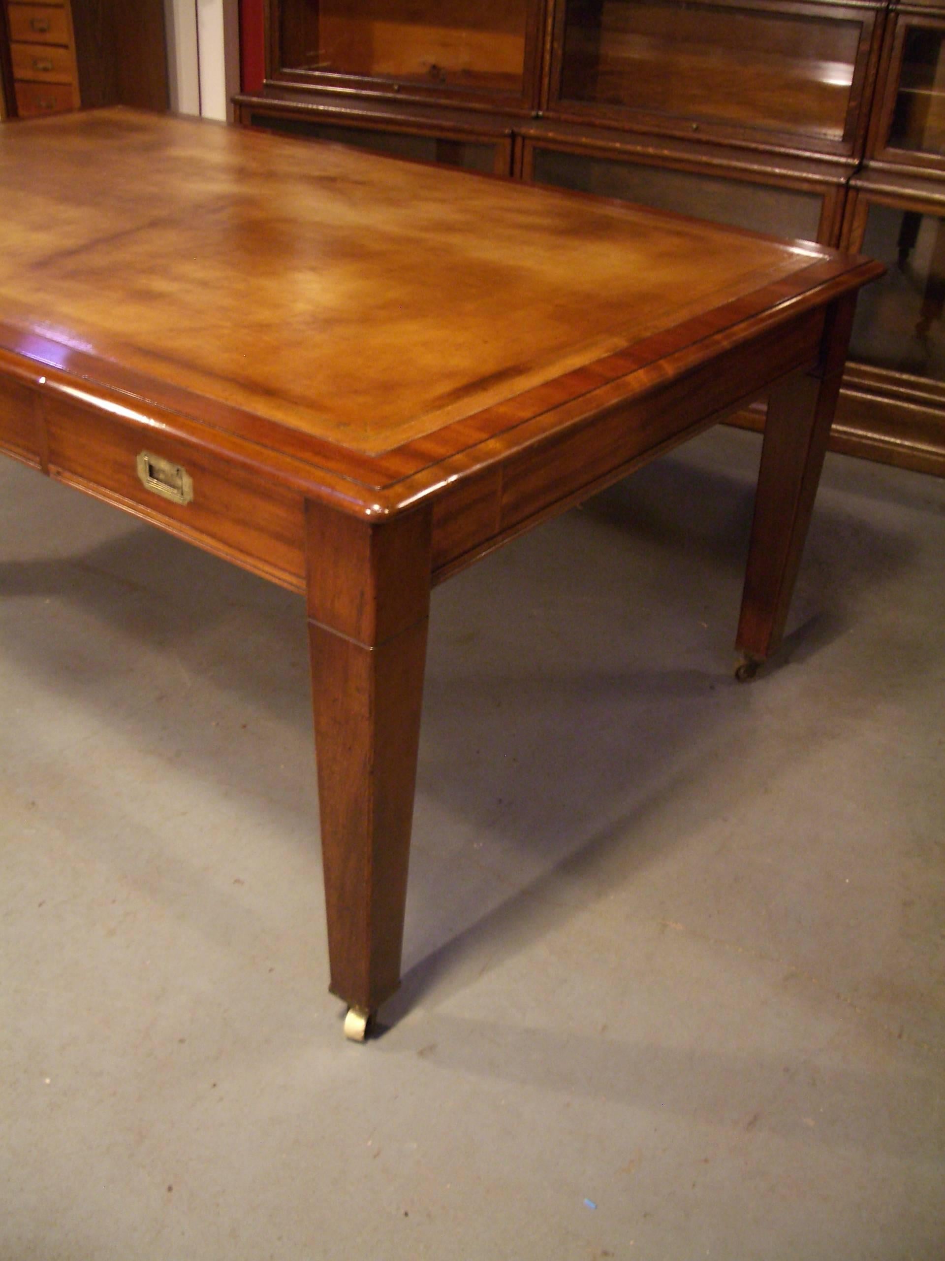 Beautiful big antique mahogany writing desk. Beautiful warm mahogany color with a tan leather (hide) top. Perfect simple look with the military handles and square tapered leg with big wheels. On both sides the table has 3 drawers. Very useful as a