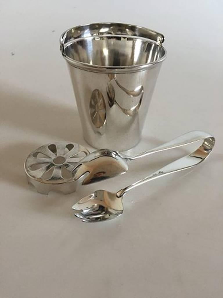A. Michelsen ice bucket with handle and ice tong in sterling silver. From 1947. Combined weight of 395 grams / 13.75 oz. The bucket measures 4 9/64 in. H. 3 15/16 in. diameter. The ice tong measures 6 11/16 in length.