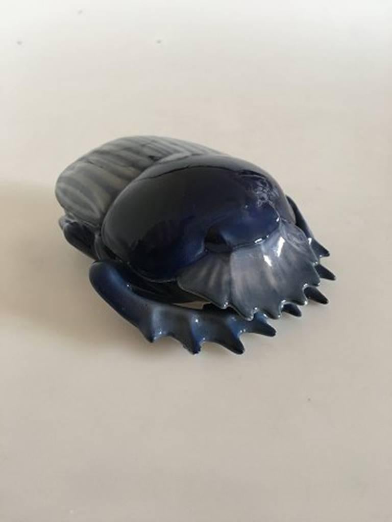 Royal Copenhagen scarab shaped lidded dish #31/16. In somewhat matte and shiny blue toned glazed finish. In beautiful whole condition. Measures 12 x 10 cm (4 31/32 in x 3 15/16 in).