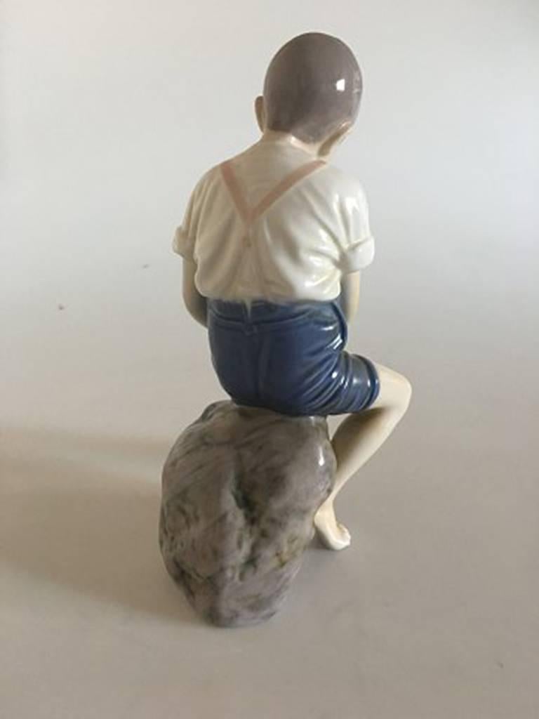 Bing & Grondahl figurine boy on stone #1757. Measures 22cm and is in good condition.