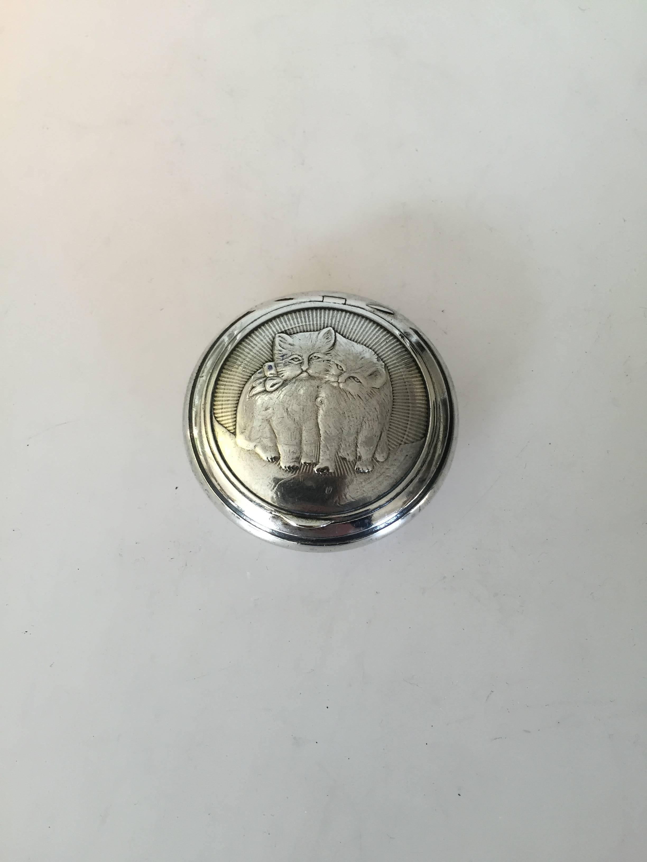 Pill and Snuff box in Silver with Cat motif. Measures 5,2cm dia. Gilded inside. Silver mark is 800 and silversmithy mark, which we can not make out. In good condition. With cat motif on the front and the back.