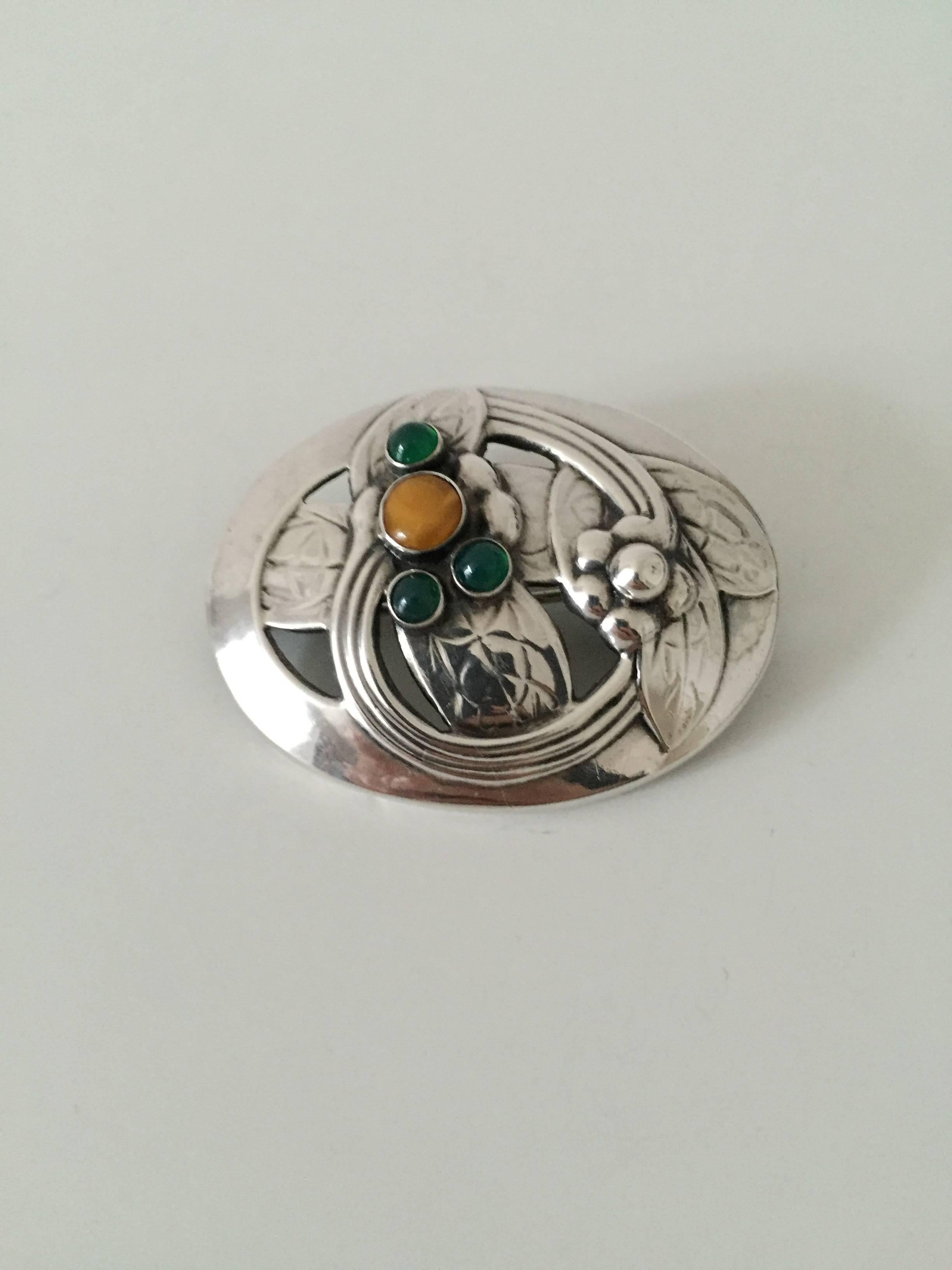 Georg Jensen sterling silver brooch #13 with amber and green stones. From 1904-1914.

Measures 5 cm x 3.9 cm (1 31/32