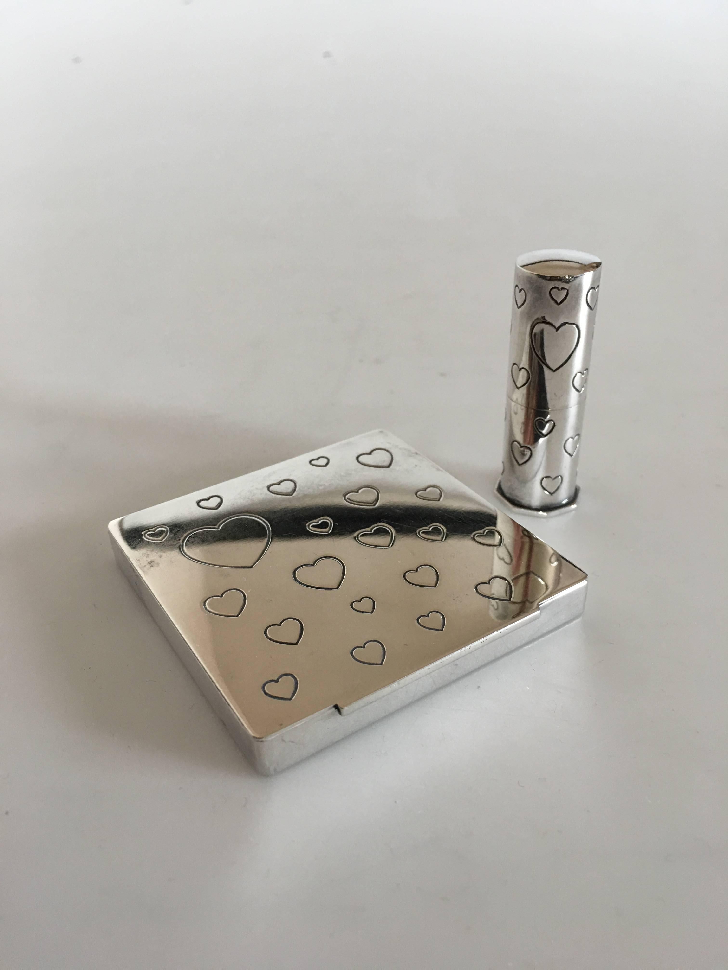 Powder and mirror case and lipstick case in silver ornamented with hearts. Without silver marks but originally purchased at Hans Hansen. Powder case measures 6.5 x 6.5 x 0.8 cm (2 9/16