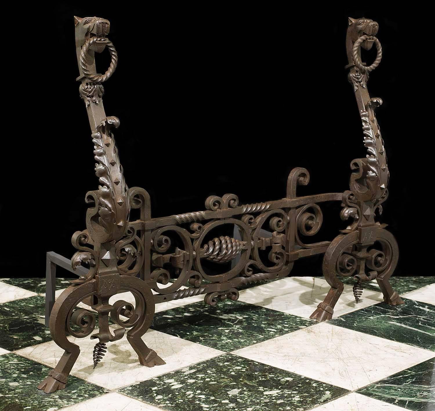 A pair of substantial Jacobean style wrought iron andirons linked by a highly ornate scrolled fender bar. The standards in the form of a pair of griffins holding rings in their mouths,
English, late 19th century. 

(Price and vat in EU zone).