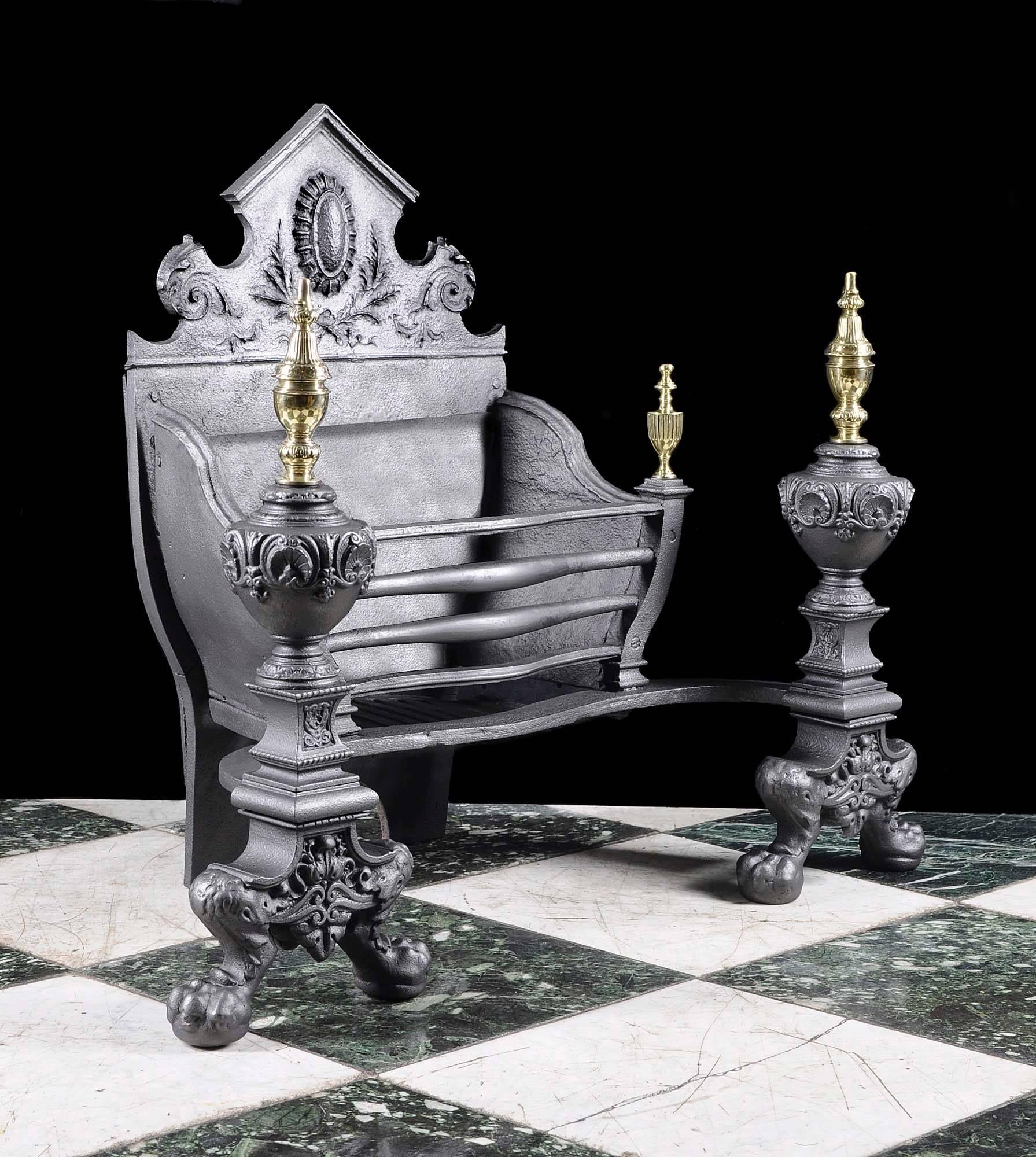 A substantial cast iron and brass Victorian fire grate, the high split pediment back centred by a boss and floral decoration in relief, the basket is supported on large elaborate baluster shaped andirons topped with brass finials above ball and claw