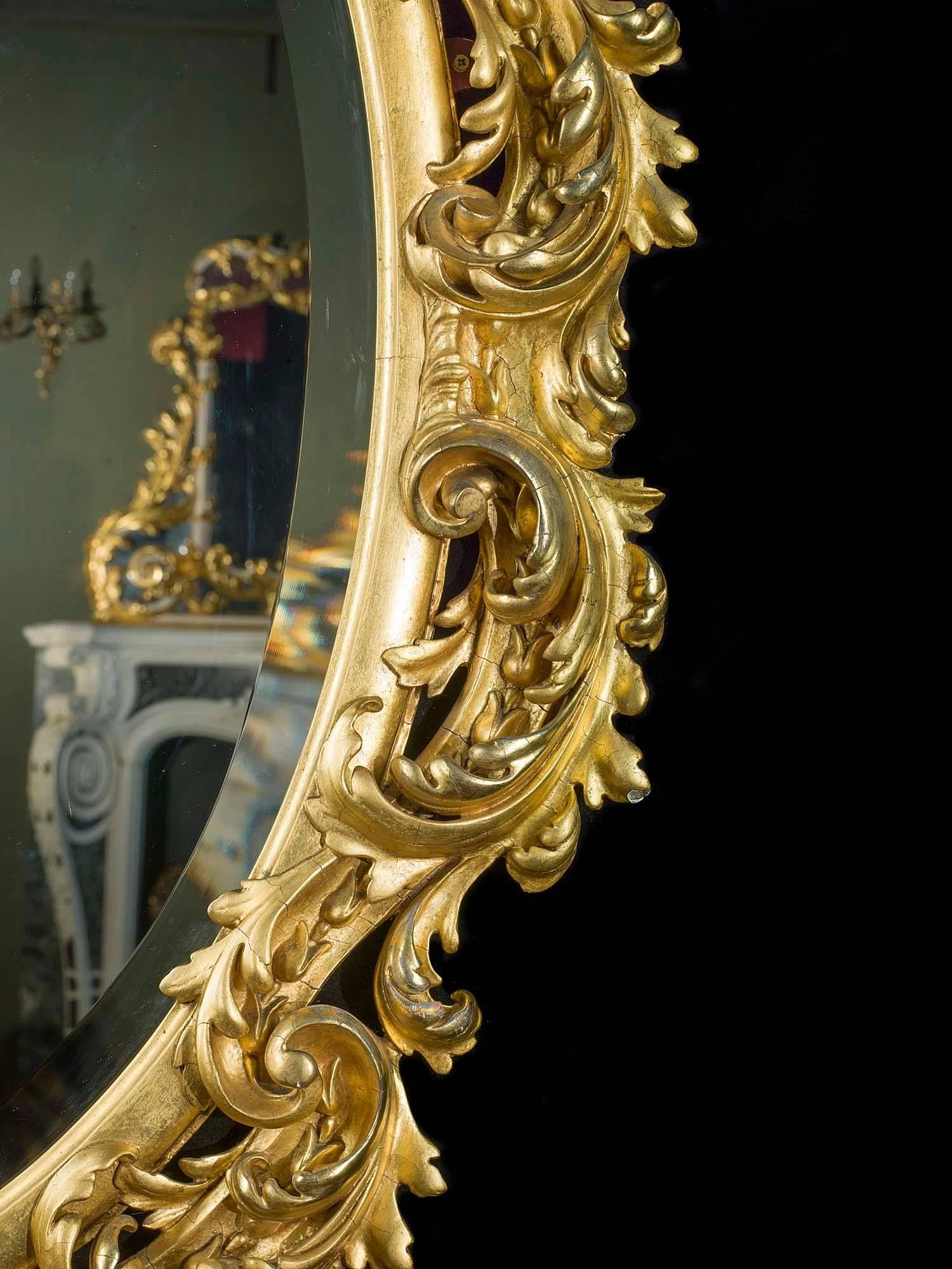 A sumptuously carved oval giltwood wall mirror, French, 19th century.