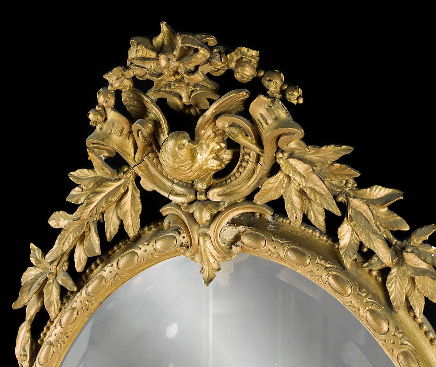 A very large oval giltwood and gesso girandole wall mirror. The mirror is topped with 
 with a bird perched within foliate ornamentation, the mirror plate set within a carved, embellished frame. This is adorned with a pair of scrolling two branch