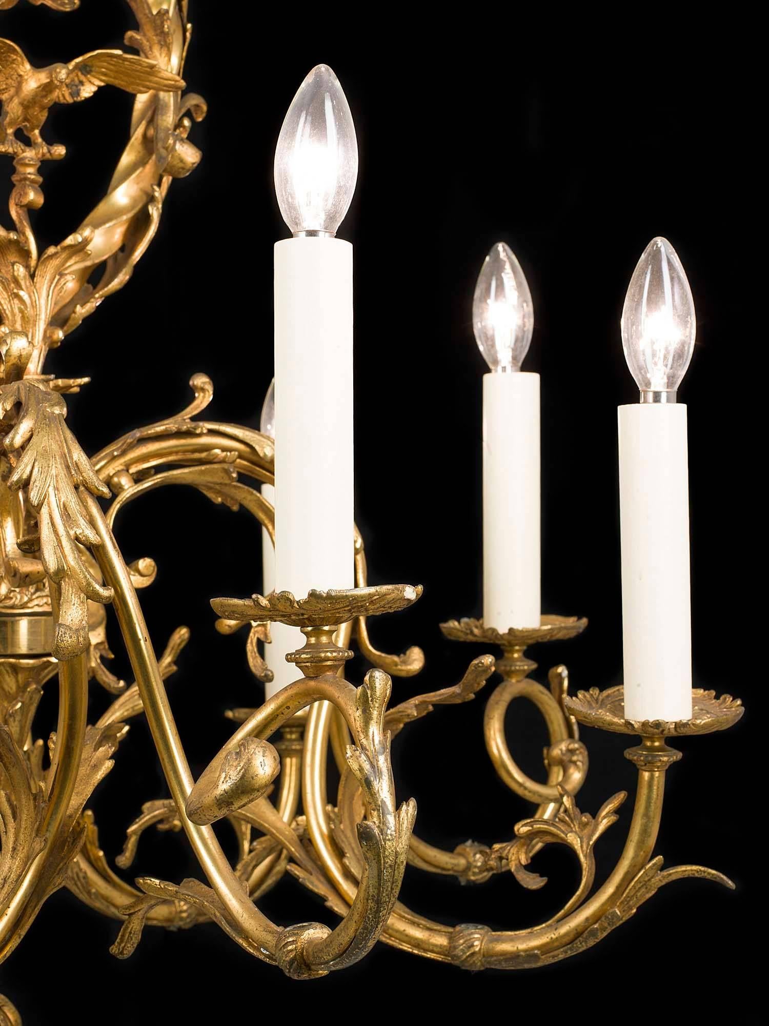 A large Rococo style gilt bronze eight branch antique chandelier which was originally made for gas but is now converted to electricity. The central barley twist scrolling stem frames a small eagle alighting onto a pedestal, and the eight scrolled