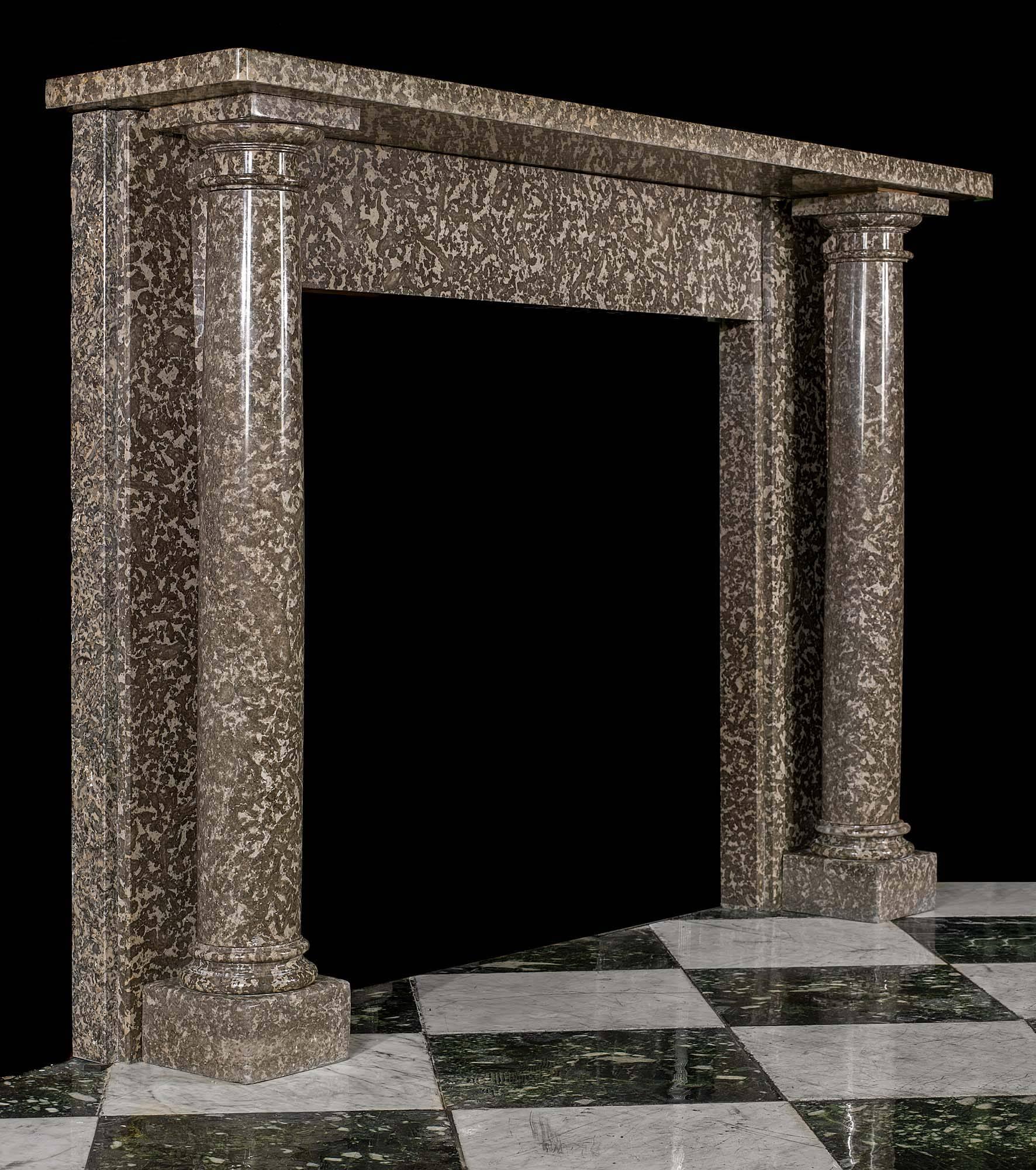 A charmingly understated Regency columned chimneypiece in warm grey fossil marble reminiscent of a leopard’s coat. The full round tapering columns stand free of the jambs and support the simple shelf set above the unadorned frieze.
English, circa