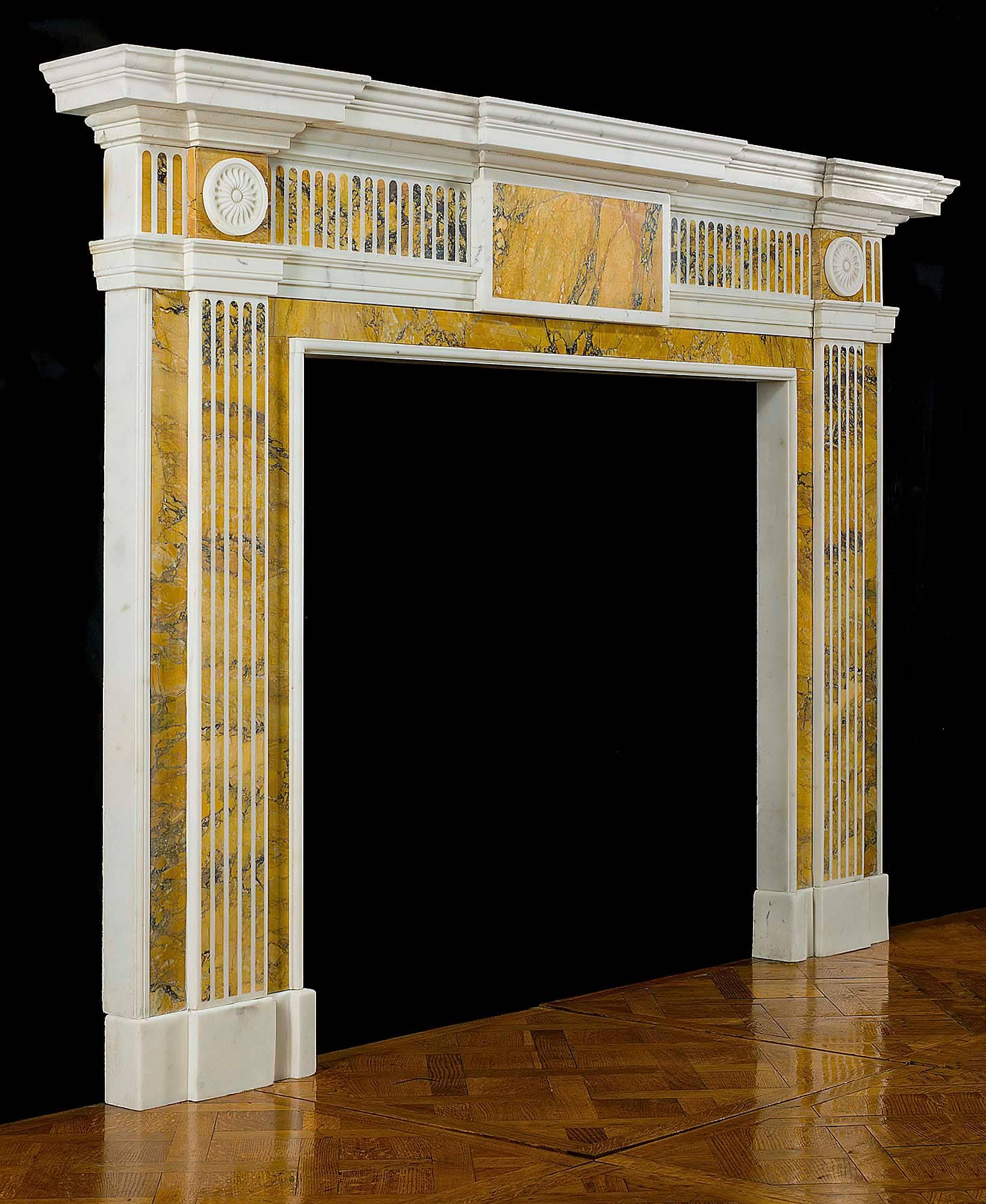 A late Georgian neoclassical chimneypiece in the manner of Robert Adam carved in white statuary marble with yellow Sienna marble inlay. The wide breakfront shelf set over the fluted frieze centered by a large tablet also of purple veined yellow