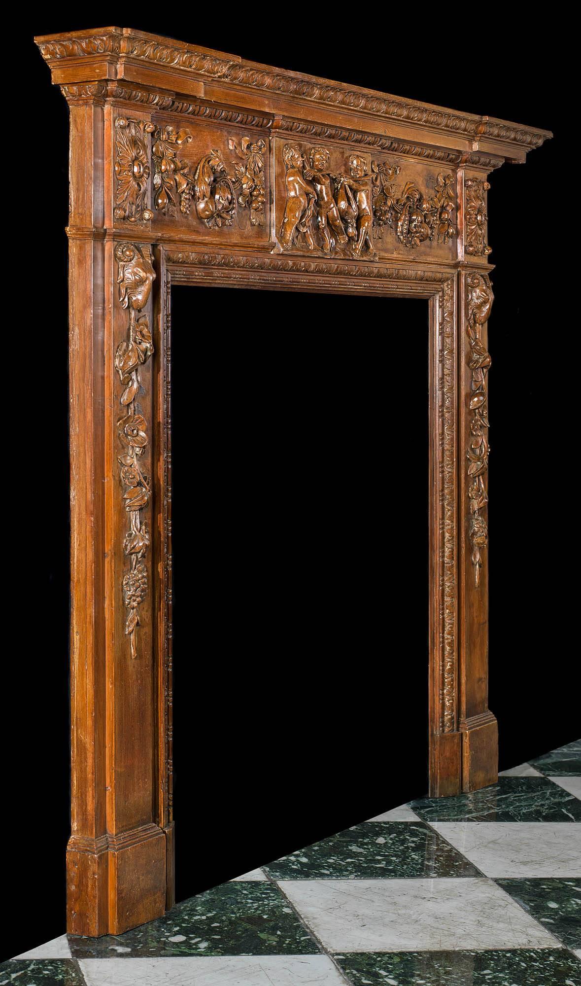 A carved pine highly decorative antique chimneypiece in the George III style.
The central plaque on the frieze, depicting three putti carrying a deer, is flanked by floral and fruiting swags.
The twin foliate paterae on the end blocks are set