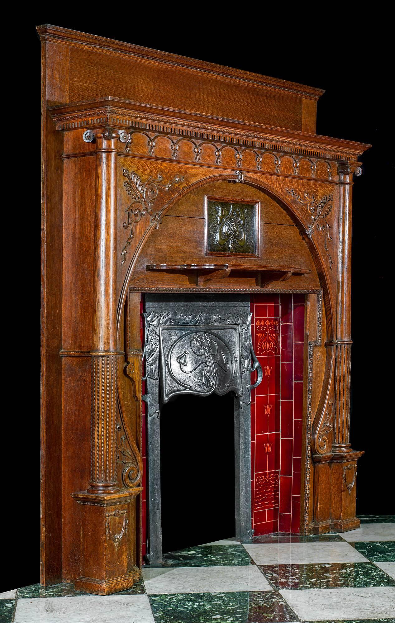 ART NOUVEAU BEAUTY
An exceptional and rare carved oak Art Nouveau chimneypiece with an integral decorative cast iron hooded insert set between two red tiled panels beneath the centred embossed copper plaque.

The carved athemion detail echoed on