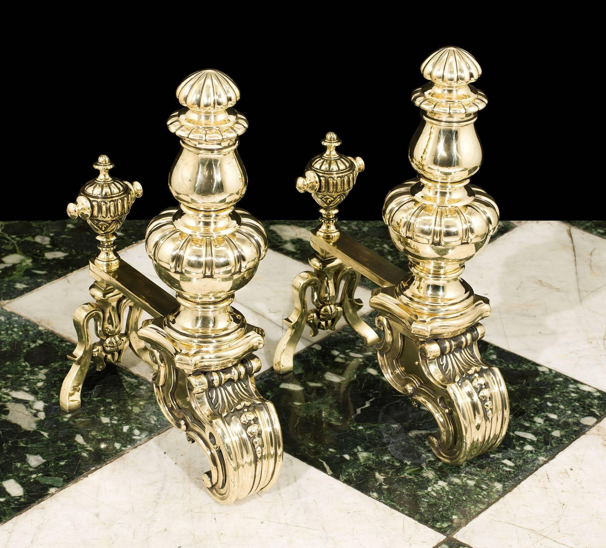 A pair of 19th century brass andirons in the French Baroque style, of fluted baluster urn shape, raised on heavy monopodic scrolled feet. The short back bars mounted by a pair of decorative urn finials and with the diamond registration mark for