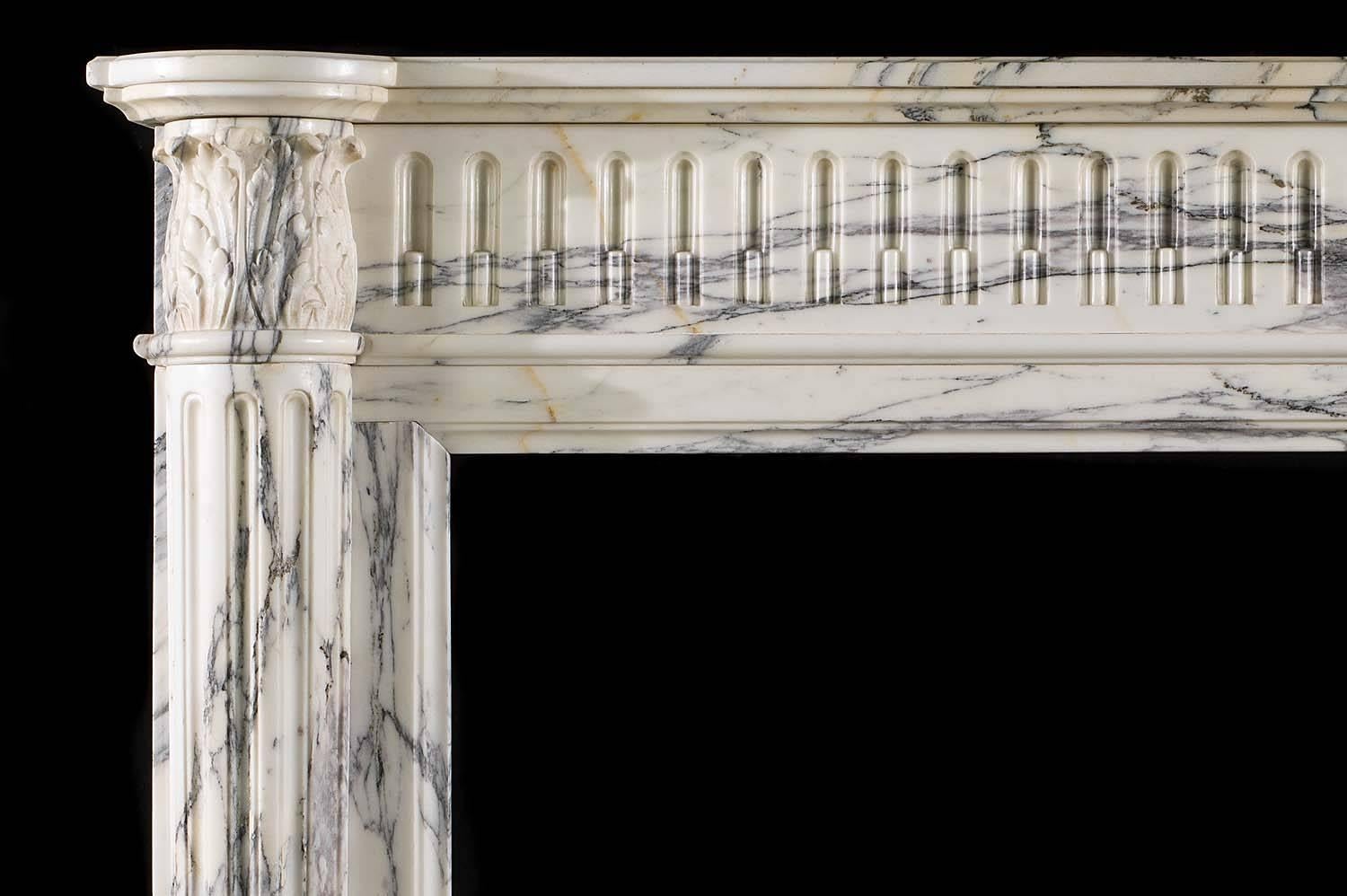 A small compact Louis XVI antique fireplace in elegantly veined Arabescato marble. The simple shelf rests over a carved stop-fluted frieze, flanked by acanthus leaf capitals supported on half round pilasters,

French, early 19th century.

(Price
