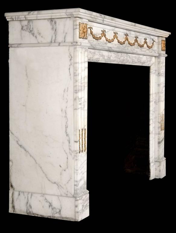 A delicate Louis XVI style veined statuary marble and gilt ormolu antique fireplace mantel. The panelled frieze with ormolu bell flower swags is flanked by square ormolu paterae end blocks, supported on stop fluted pilaster jambs decorated with