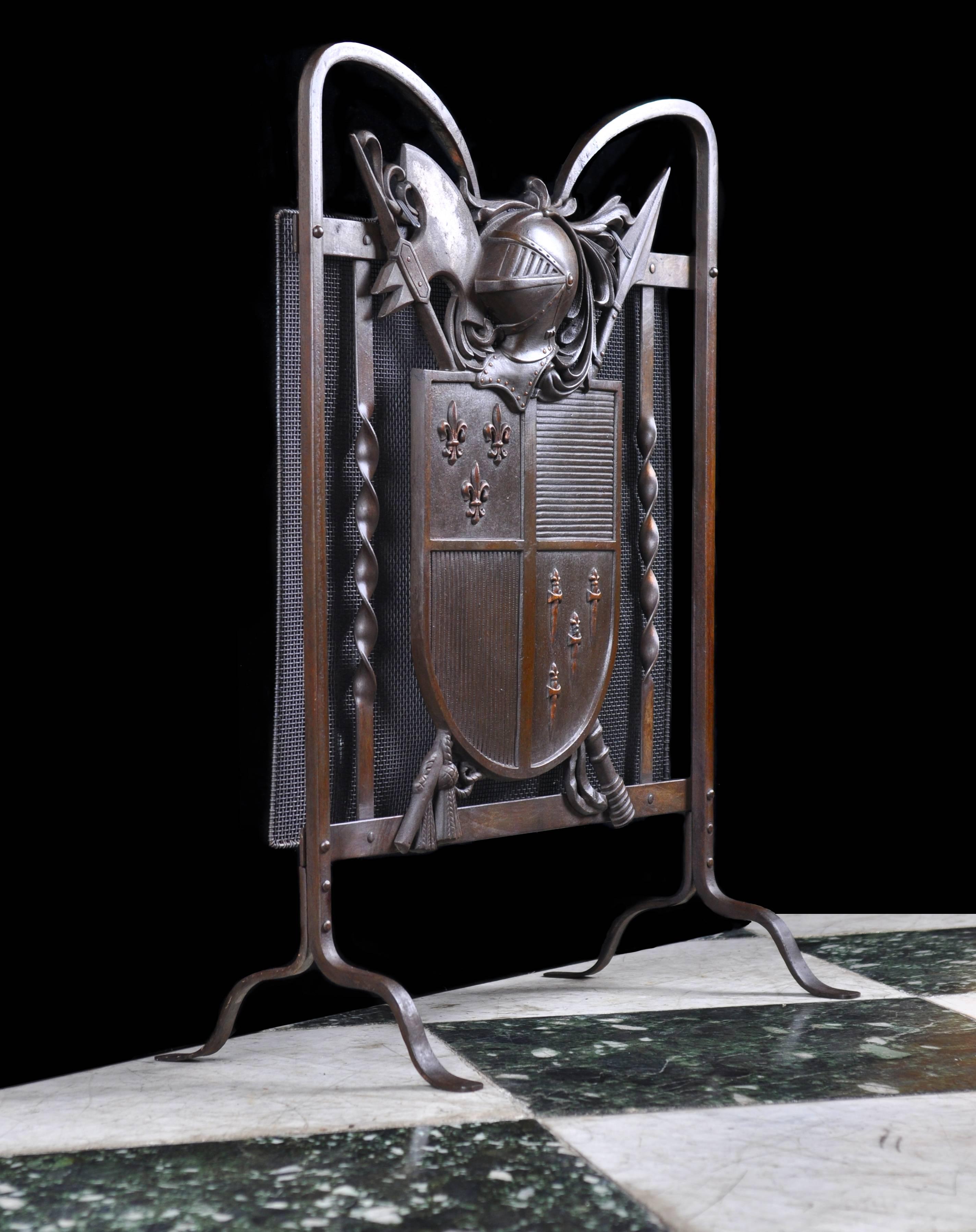 An armorial fireguard of bronze, wrought and cast iron featuring a medieval knight's helmet and a crossed halberd and spear behind a shield with fleur-de-lys and daggers in the quarter panels. Cast in the back are the words - Nestor British Made