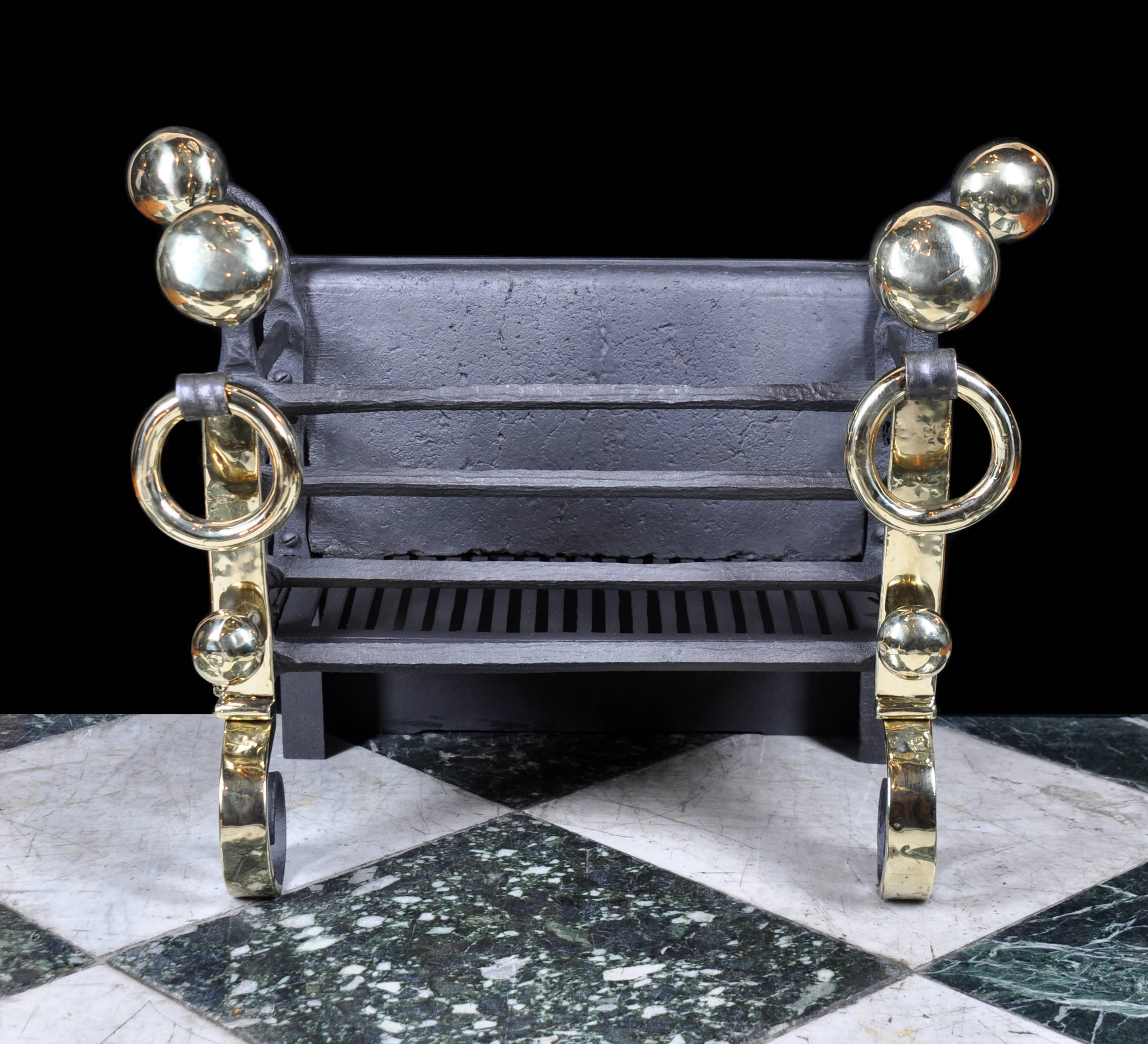 A late 19th century Arts & Crafts fire grate in wrought iron with large brass disc finials behind brass rings above scrolled feet. 

English, circa 1890.
 