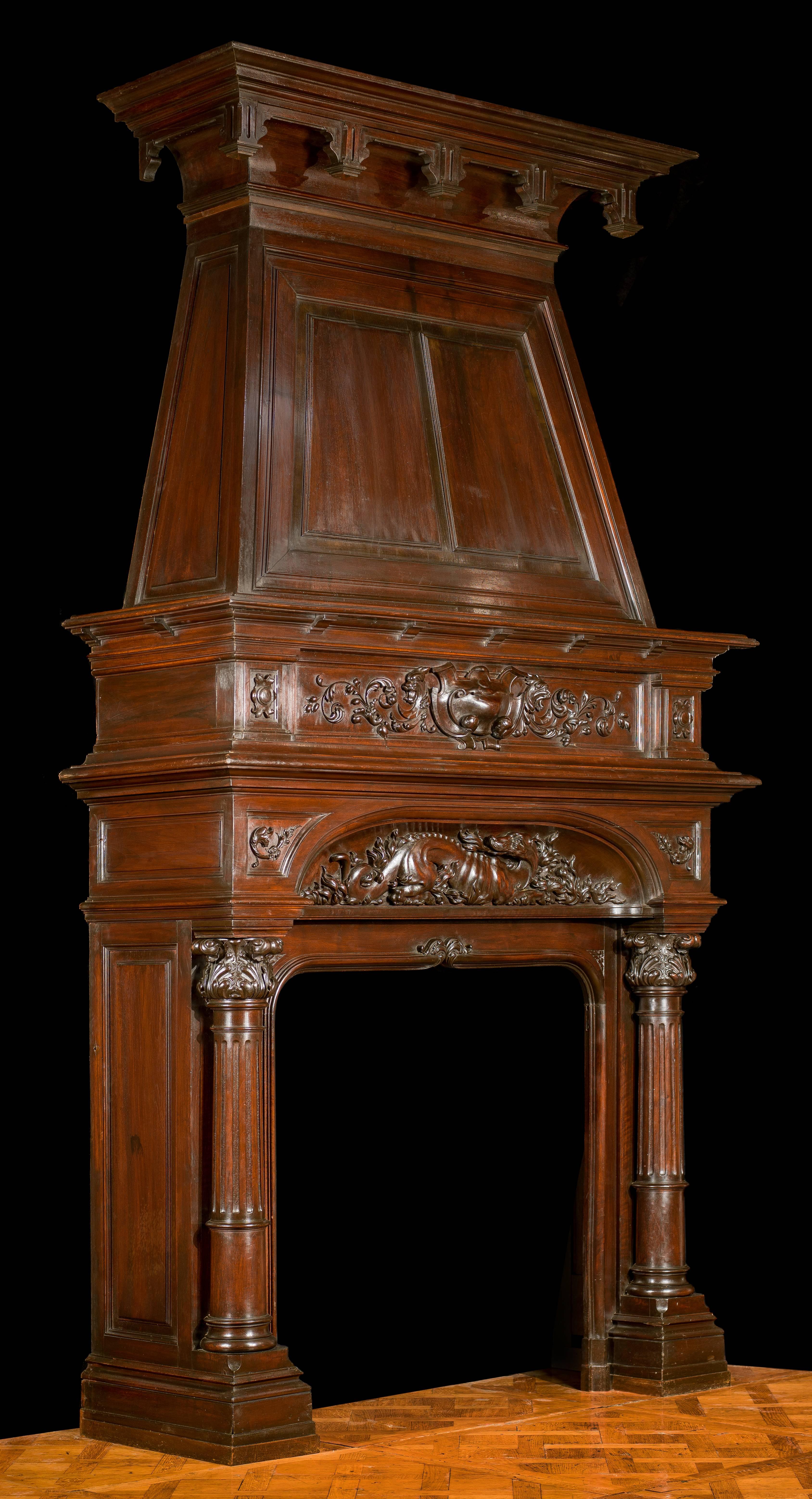 A tall and boldly carved, columned walnut trumeau fireplace in the Renaissance style. The upper frieze, with a central cartouche flanked by floral scrolls, is set above the main frieze upon which is carved, in high relief, a fire breathing