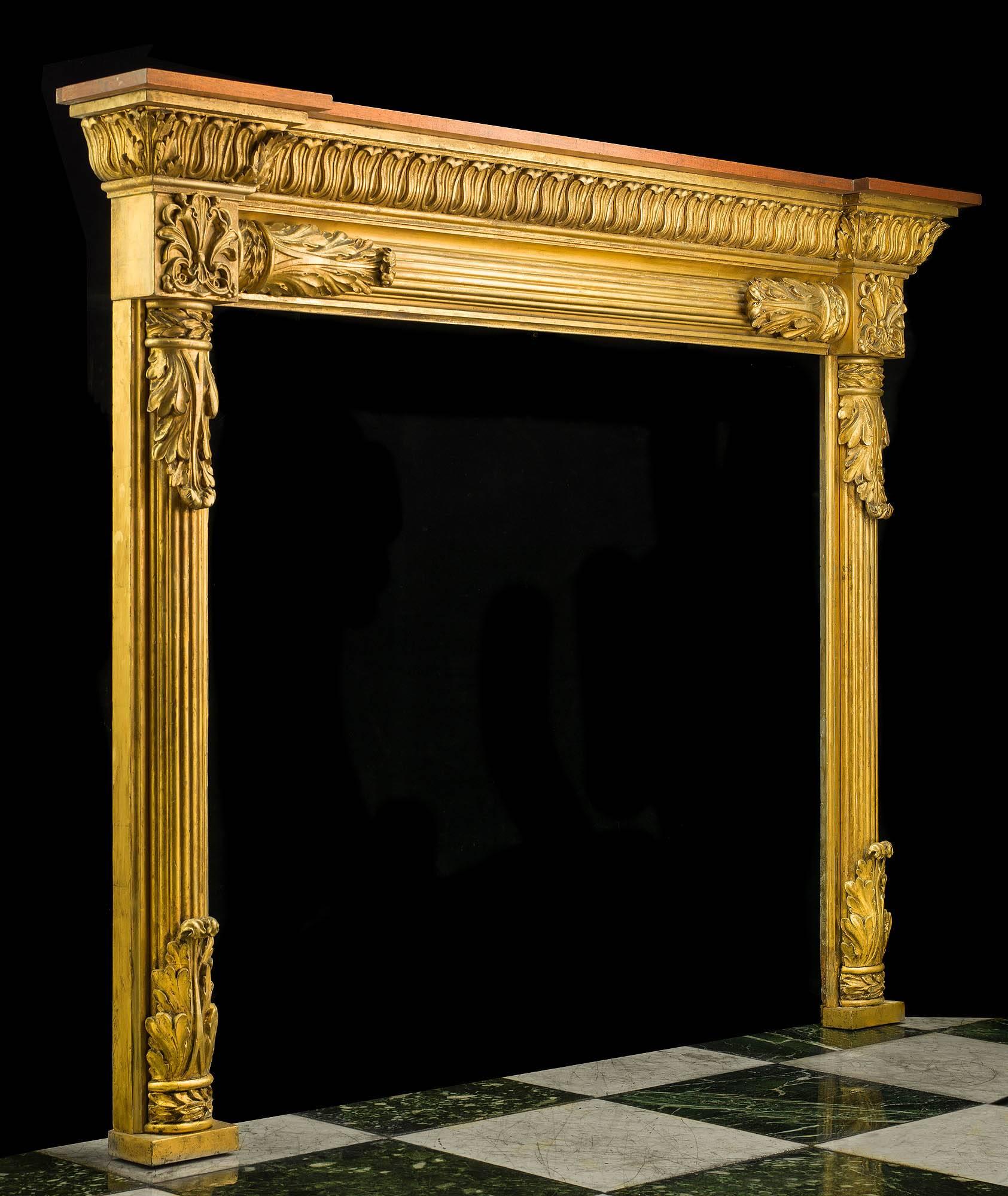 Une très belle cheminée anglaise de style Régence en pin sculpté, acajou et bois doré de composition. L'étagère du fronton en acajou est surmontée d'un motif de langue d'agneau richement sculpté, la frise est cannelée avec des terminaisons en