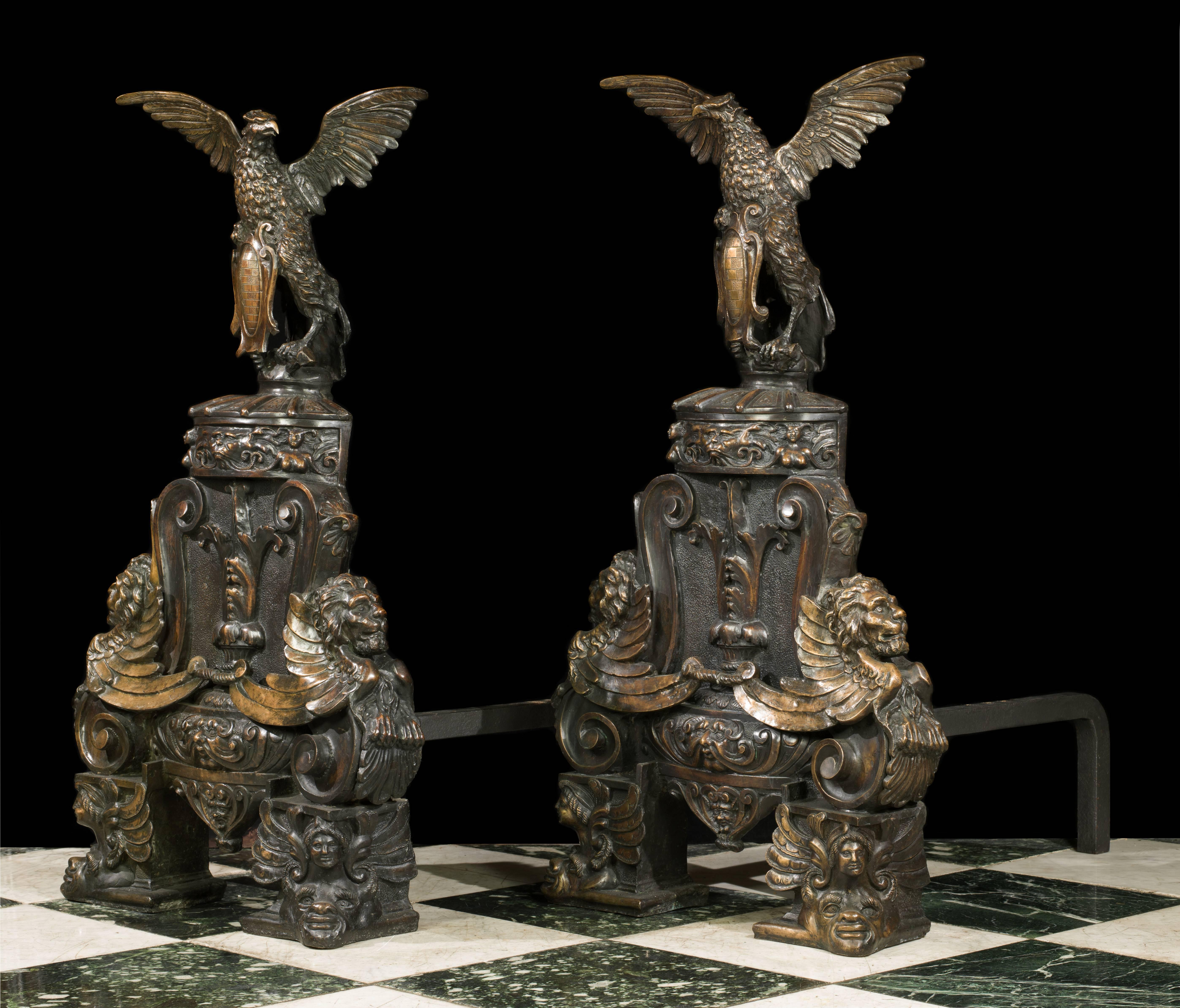 A pair of enormous and rather eccentric patinated bronze andirons in the Baronial Baroque manner. Each is surmounted by majestic spread winged eagles holding scrolled cartouche shields and perched on ornate drums decorated with mythical beasts and
