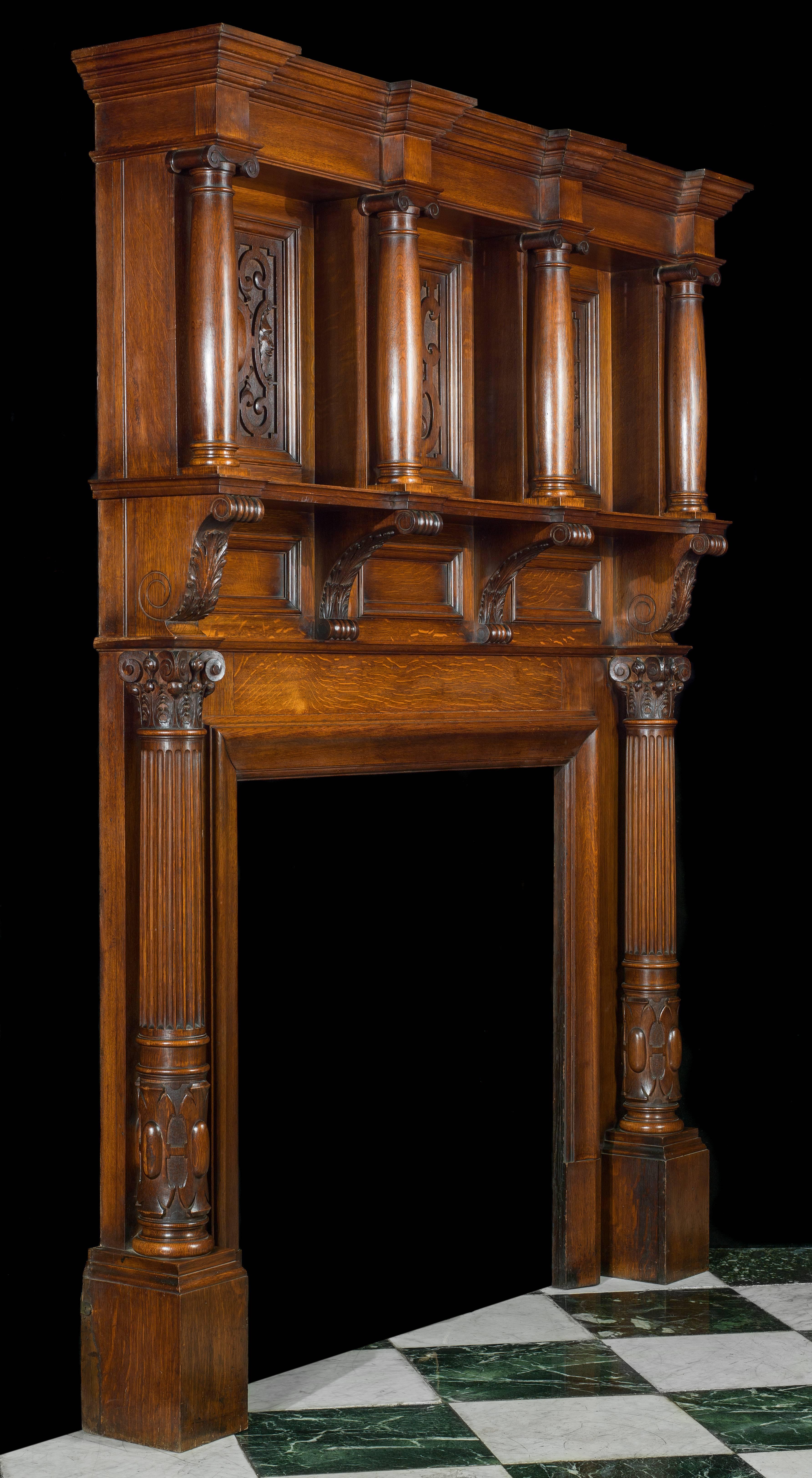 An Edwardian carved oak antique fireplace surround and overmantel in the Jacobean manner. The breakfront corniced top rests on four free standing oak columns behind which are three large strapwork panels set above three plainer panels divided by