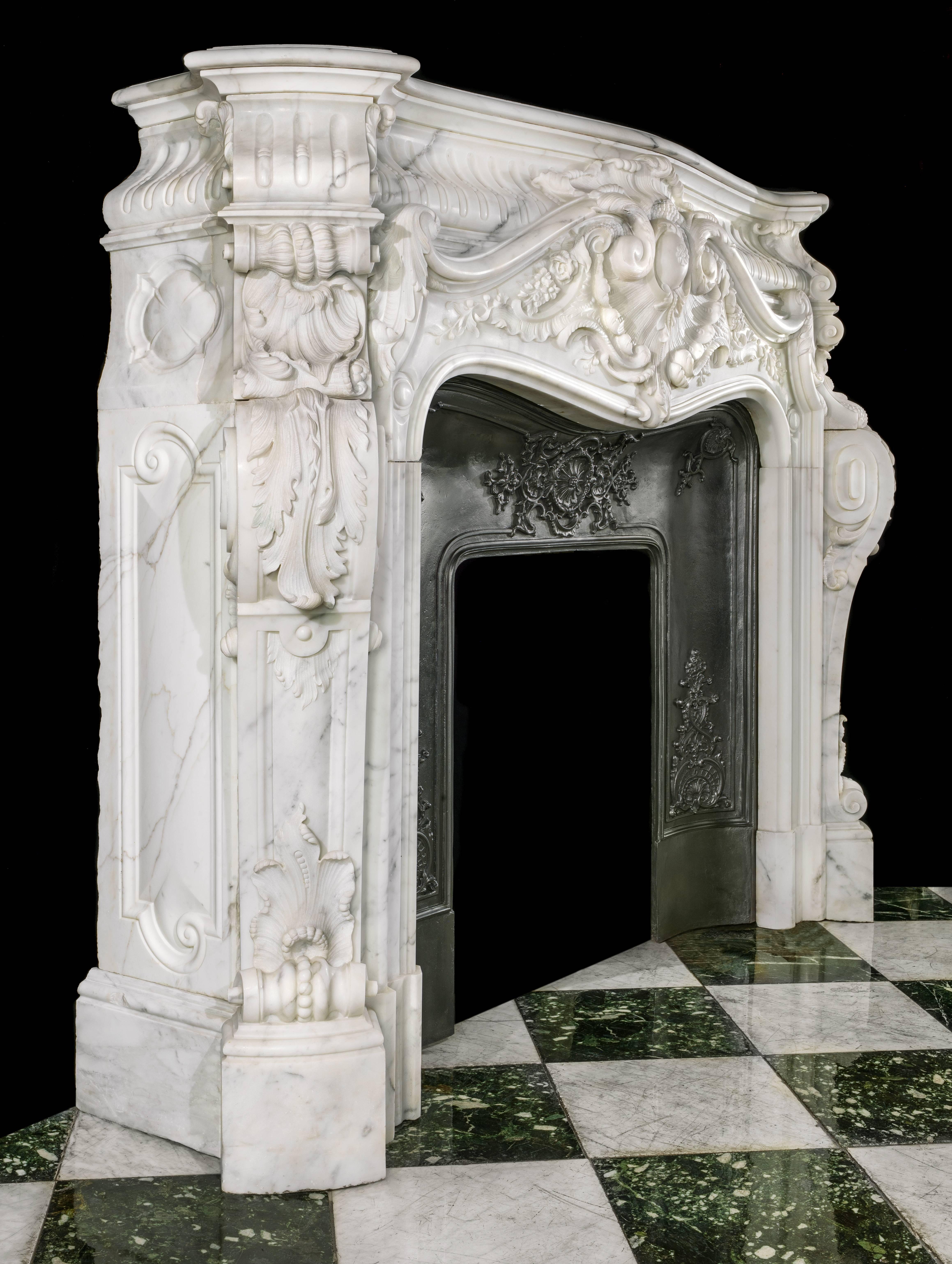 A rare, monumental and highly ornate Louis XV style deeply carved statuary marble antique fireplace surround with it's original cast iron insert. The upper stop fluted coffered frieze sits above and behind an enormous and most elaborately scrolled
