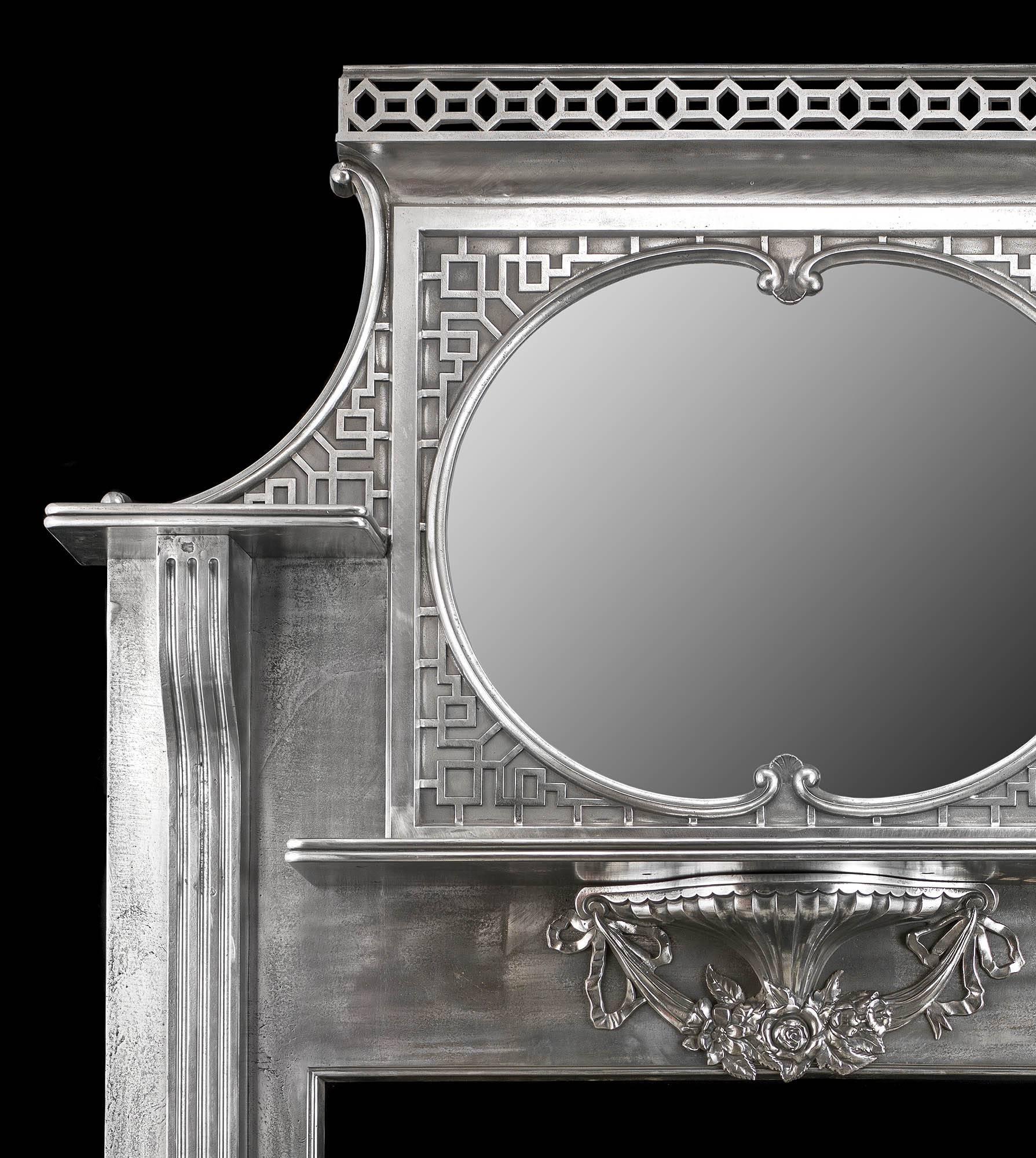 An exceptional Edwardian Chinese Chippendale style cast iron antique fireplace surround and integral overmantel. The overmantel, with a pierced fretwork crest, is set above a mirror surrounded by a blind fretwork geometric decoration with a shelf to