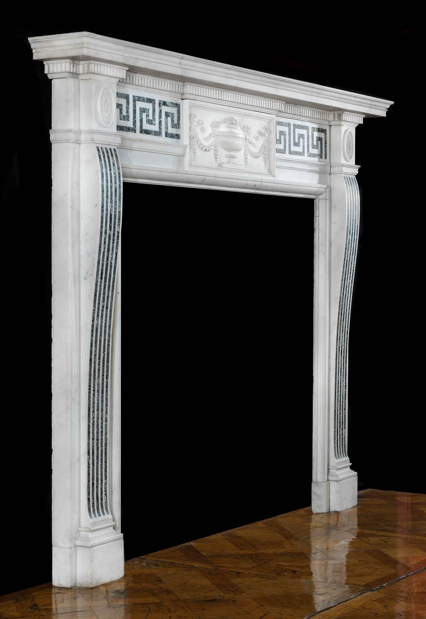 A refined and elegant Edwardian neoclassical style antique fireplace, in white statuary marble inlaid with Verdi Antico. The central plaque is decorated with a finely carved urn surrounded by bell flower swags tied with ribbons. The inlaid Verdi