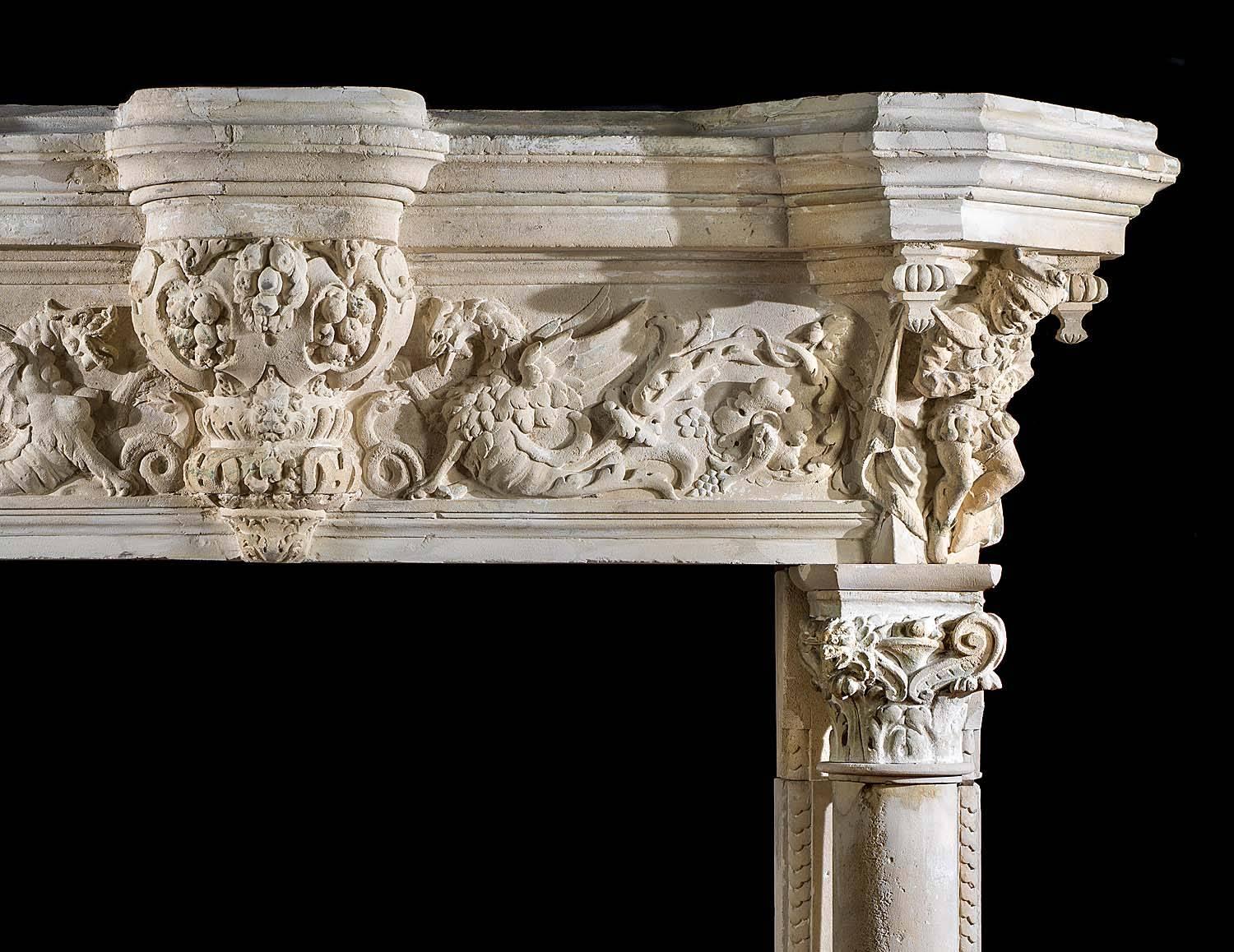 A monumental French Renaissance style antique chimneypiece highly carved in creamy Caen Stone. The massive entablature, with its breakfront shelf centred by a podium above cherubs and grotesque masks, has a boldly carved frieze of mythical dragons