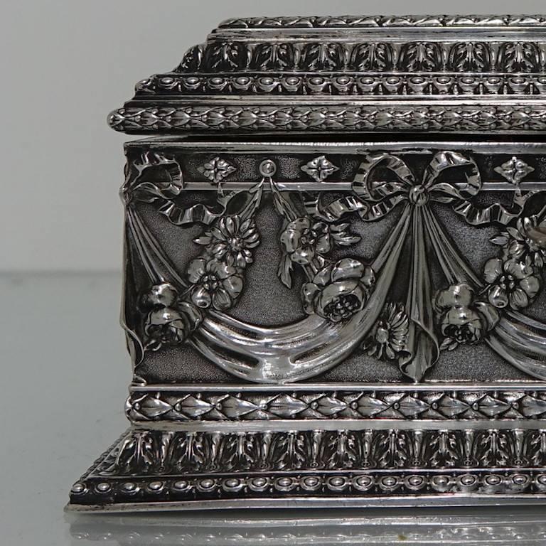 A very good quality solid base silver jewelry casket with pink inlay velvet. The workmanship on the body of the box is set on a matte background with garlands entwined with floral hanging wreaths. The lid of the box has a scene of cherubs at work.