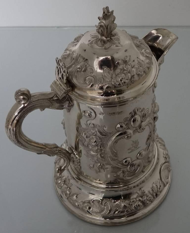 A strikingly beautiful large flagon elegantly embossed throughout. The flagon has an ornate cartouche with a family crest depicting a unicorn. The lid is hinged with a floral finial. The handle is single scroll with an added thumb piece for easy