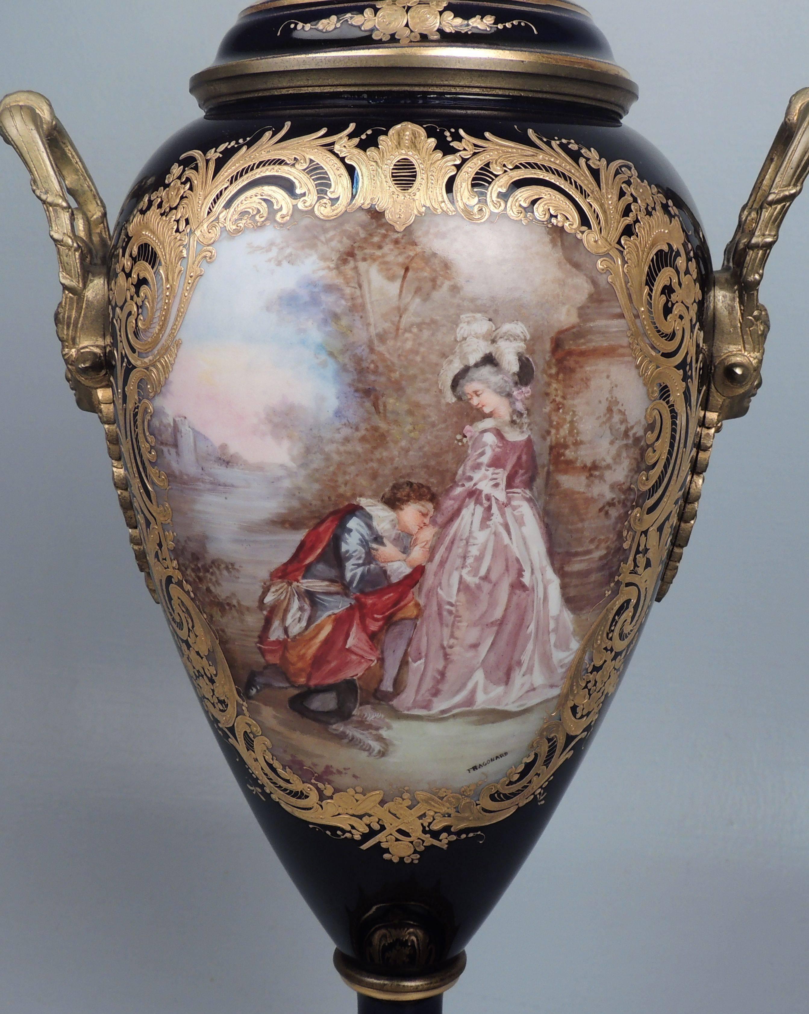 A good, large, Sevres-type, bronze mounted porcelain urn. 

Cobalt blue glazed and heavily gilded, the porcelain urn has two opposing hand-painted cartouches. The front cartouche bears a signature for Fragonard. 

The base and lid interior both