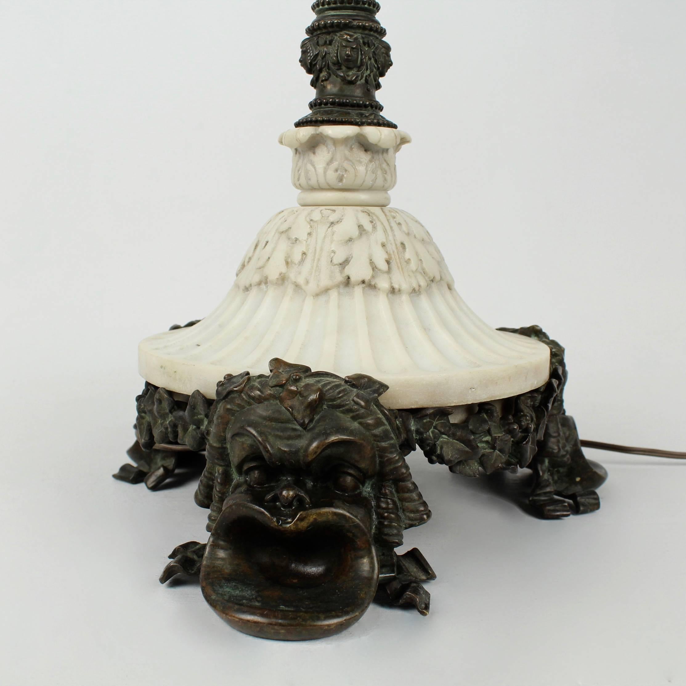 An antique E. F. Caldwell bronze and marble table lamp of exceptional quality. 

Feet modeled as Greek masks support a round carved, fluted white marble base and a cast bronze central pedestal for the lamp. 

The lamp was likely originally