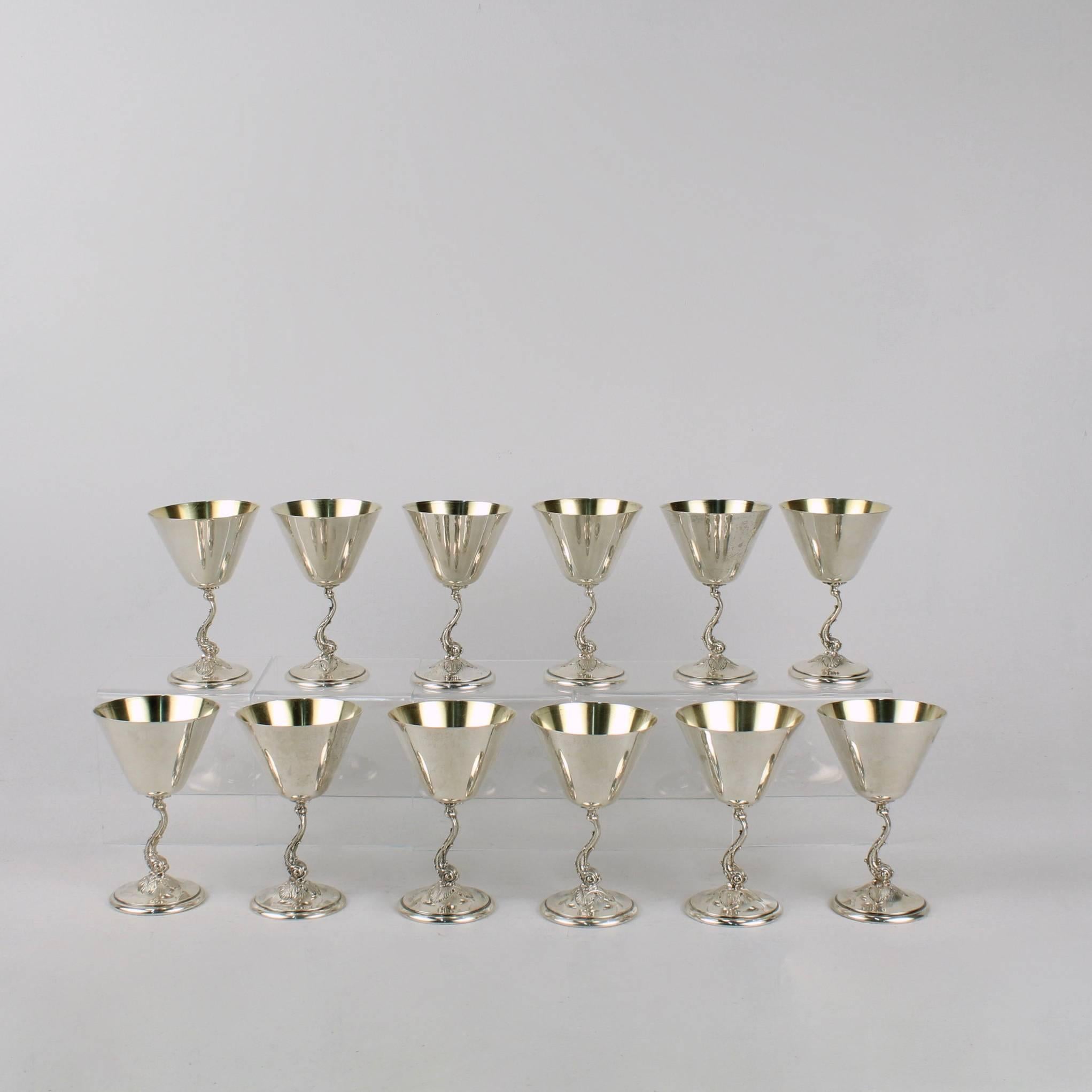 A complete set of 12 Art Deco sterling silver martini or cocktail goblets.

Manufactured by Redlich & Co of New York, New York and retailed by Gorham Inc.

Each cup is supported by a cast figural dolphin-form stem that rests on an engraved round