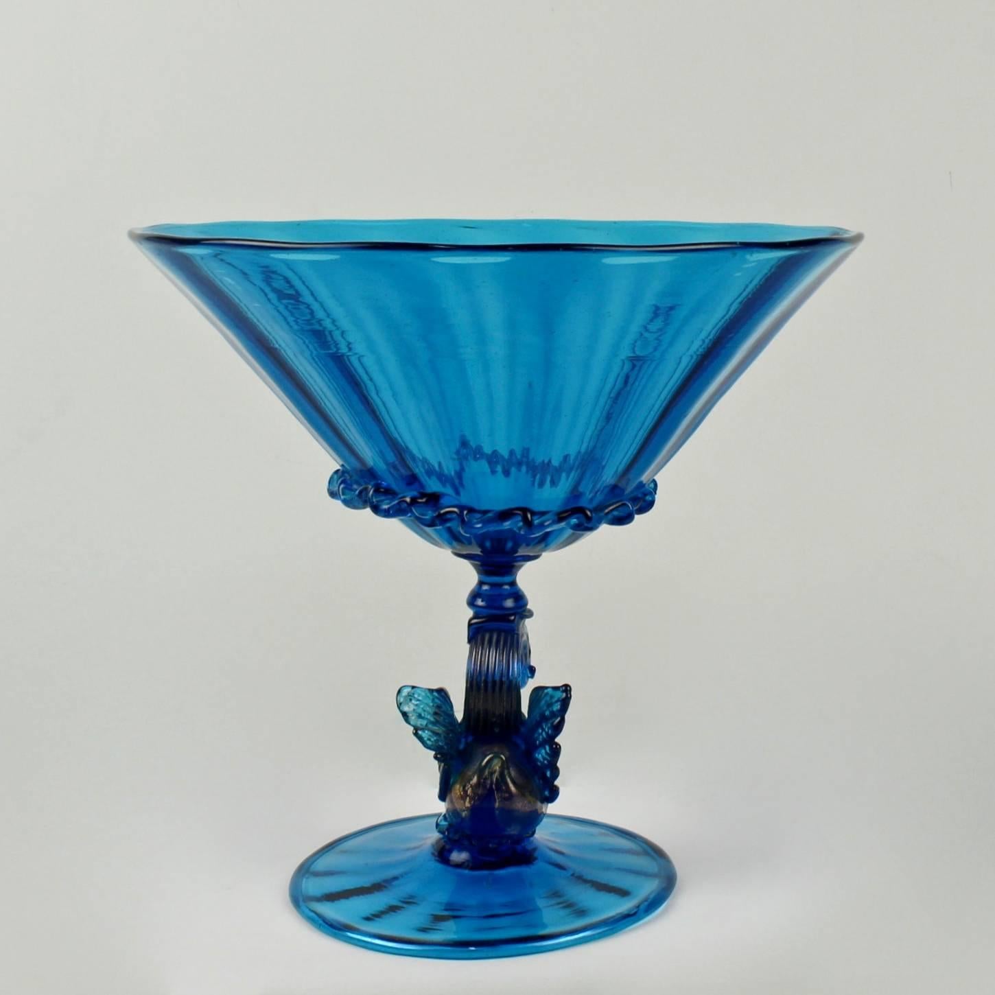 A large blue venetian glass footed bowl.

Likely Salviati with ribbed swirl design in the bowl and footed, applied rigaree band to the bowl, and a figural swan support with gold fleck. 

The bowl has a slight lean to one side, and the base has a