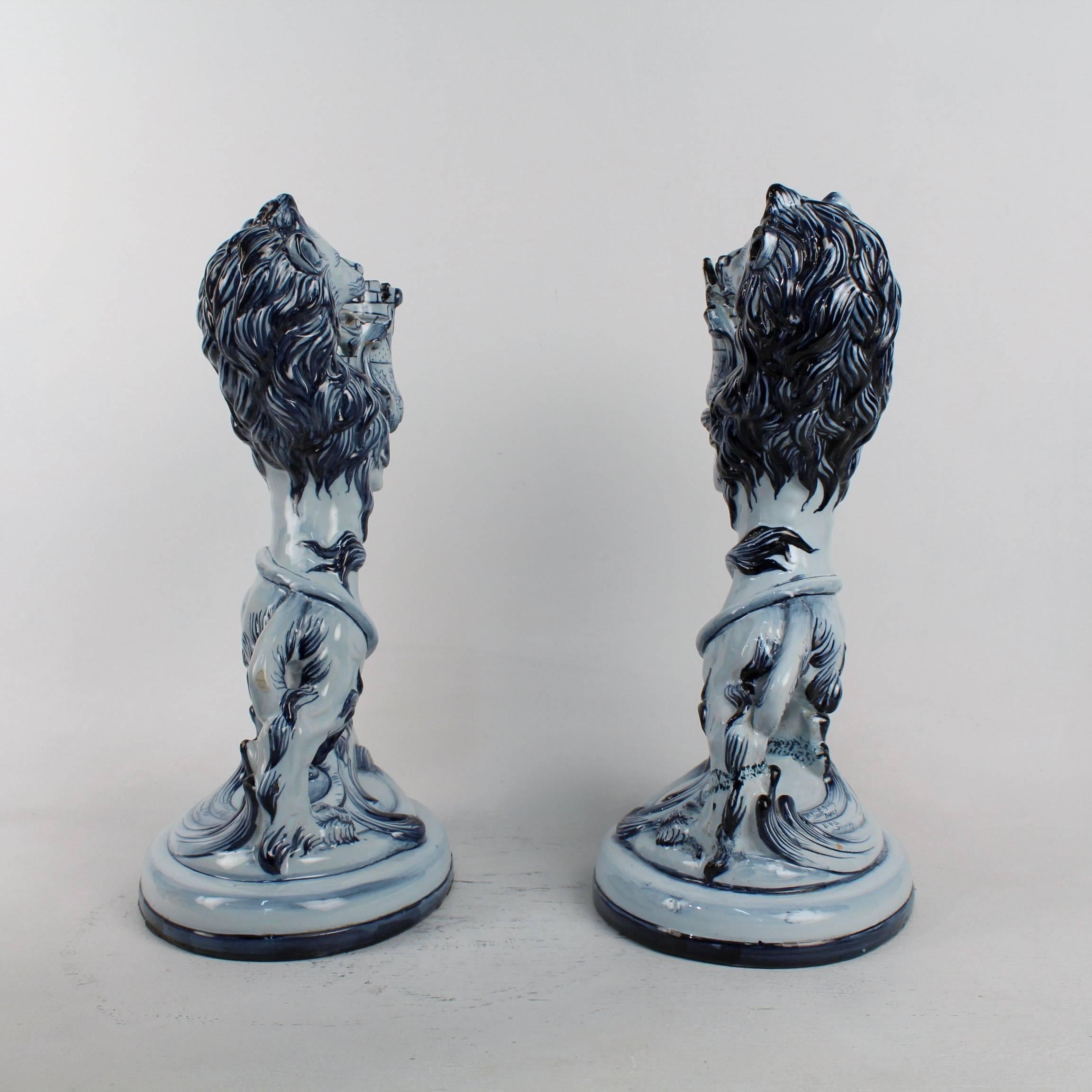 A matched pair of late 19th century Émile Gallé faience lions in blue. 

The lions are modeled standing erect on two feet holding a castle tower in their paws. They can serve as candlesticks, candelabra bases, or mantel garniture pieces.

Each
