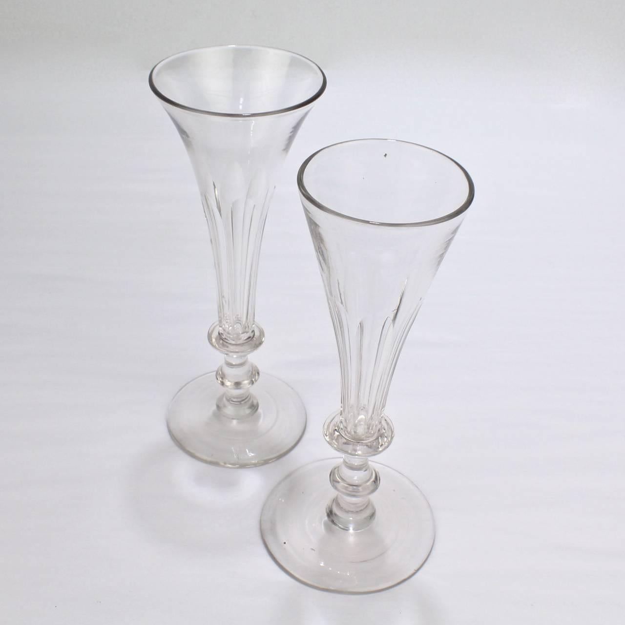 A fine, near pair of early Regency Period Anglo-Irish glass champagne flutes.

Two fine handblown examples with faceted, trumpet form flutes supported on a stems with angular knops and a wafer feet. Each with charming signs of handmade production
