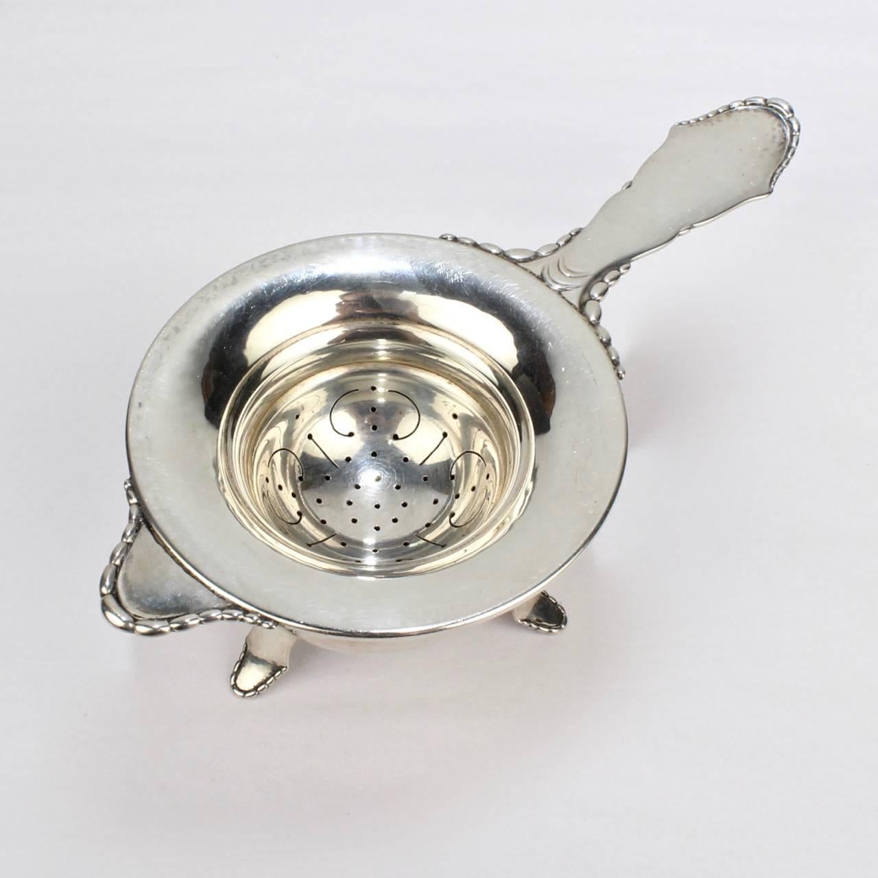 A fine Art Deco period Danish hand-hammered sterling silver tea strainer and Stand.

The design is typically Danish with a beaded edge, visible Hammer marks, and a hint of Georg Jensen style.

Made by the noted Grann and Laglye silversmiths in