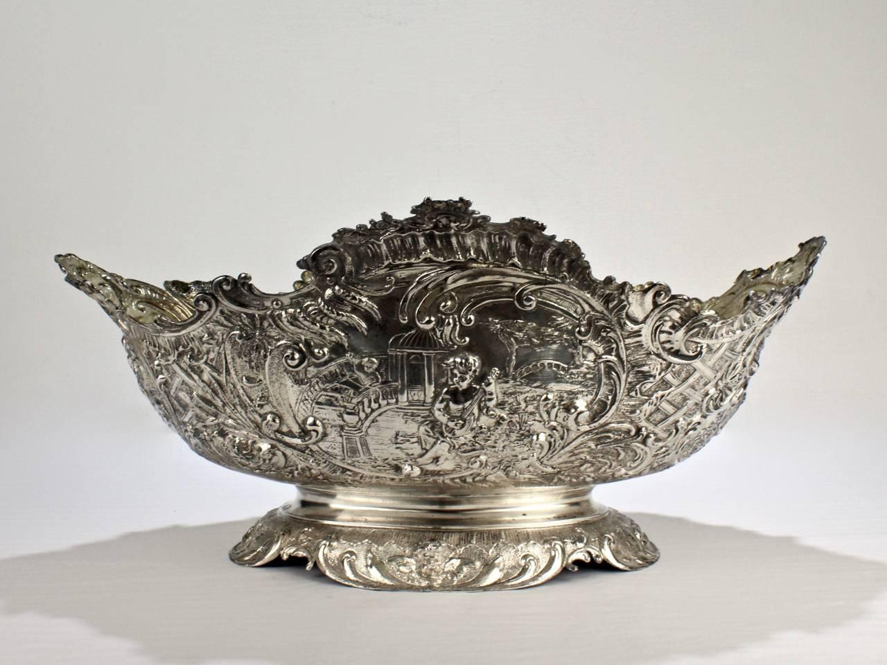 A large-scale, extremely ornate 19th century Rococo Revival solid silver bowl or centrepiece. 

Constructed of worked and fused sections each having large cartouches. 

Each cartouche has scenes of cherubs and a faux basket weave decoration. 

The