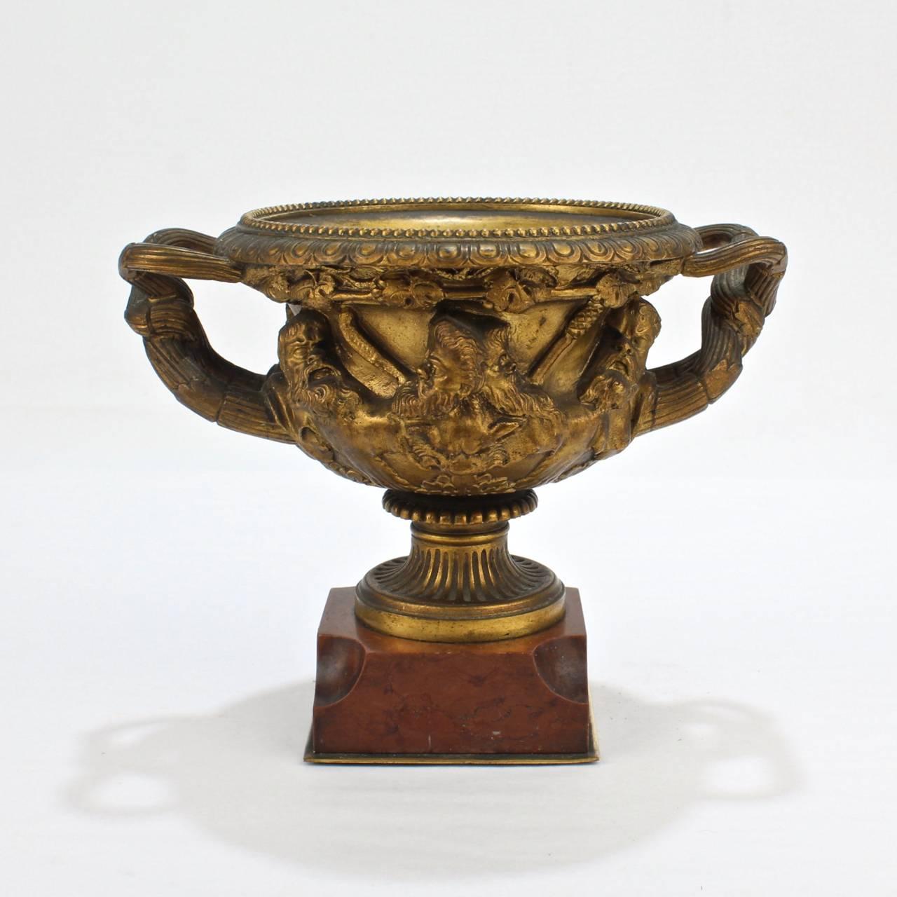 A diminutive, cabinet size gilt bronze Warwick vase.

The twin handled urn form vase is perfectly scaled for the desk or curio cabinet.

This vase is modeled after the ancient marble vase discovered in Hadrian's Villa, which is now housed in the