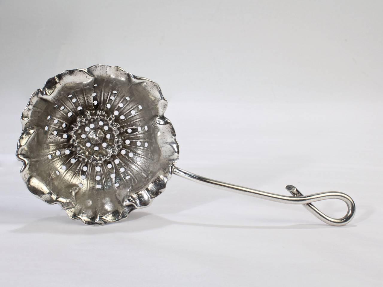 A fine antique American sterling silver figural tea strainer manufactured by George Shiebler & Co.

With the bowl modeled as an inverted poppy flower attached to a handle with looped end.

Reverse bears the Shiebler factory mark, Sterling, and