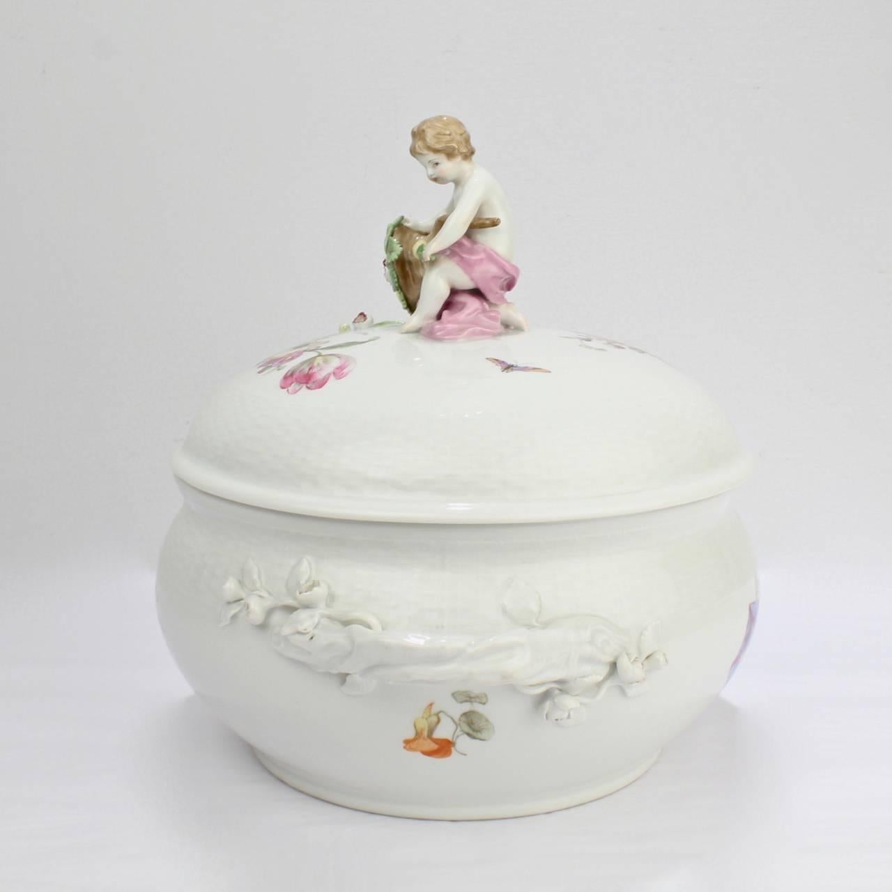 A fine antique KPM porcelain tureen with flower encrusted handles, Deutsche Blumen floral sprays, and a figural cherub and cornucopia finial. 

The base bears a blue underglaze factory scepter mark, an iron-red orb mark, and iron cross mark, and
