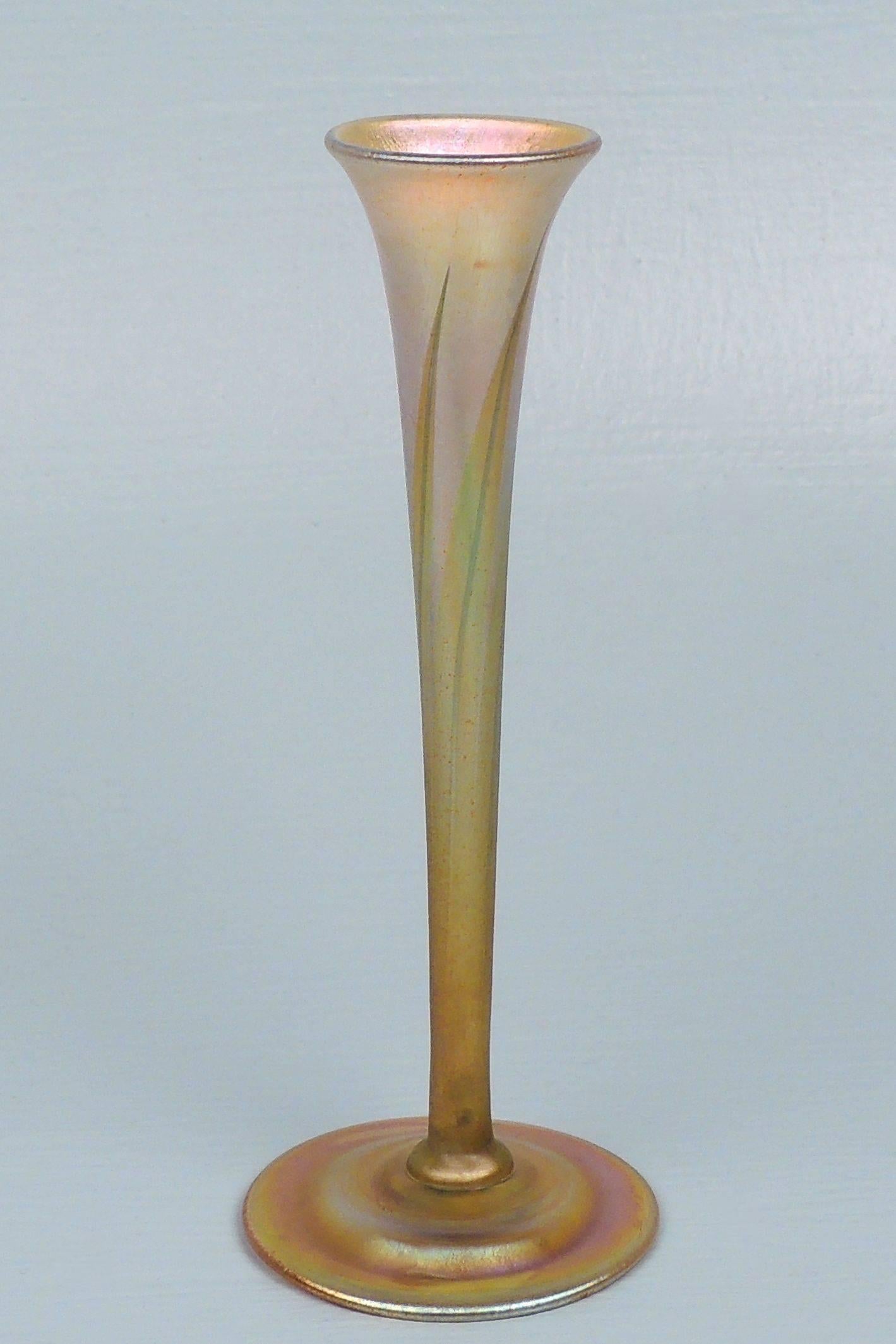 An elegant Tiffany Favrile art glass bud vase with iridescent pulled feather design. The color shifts from platinum above to an orange at the base and foot.
The trumpet form top sit slightly askew on a round foot and evidences the spontaneous