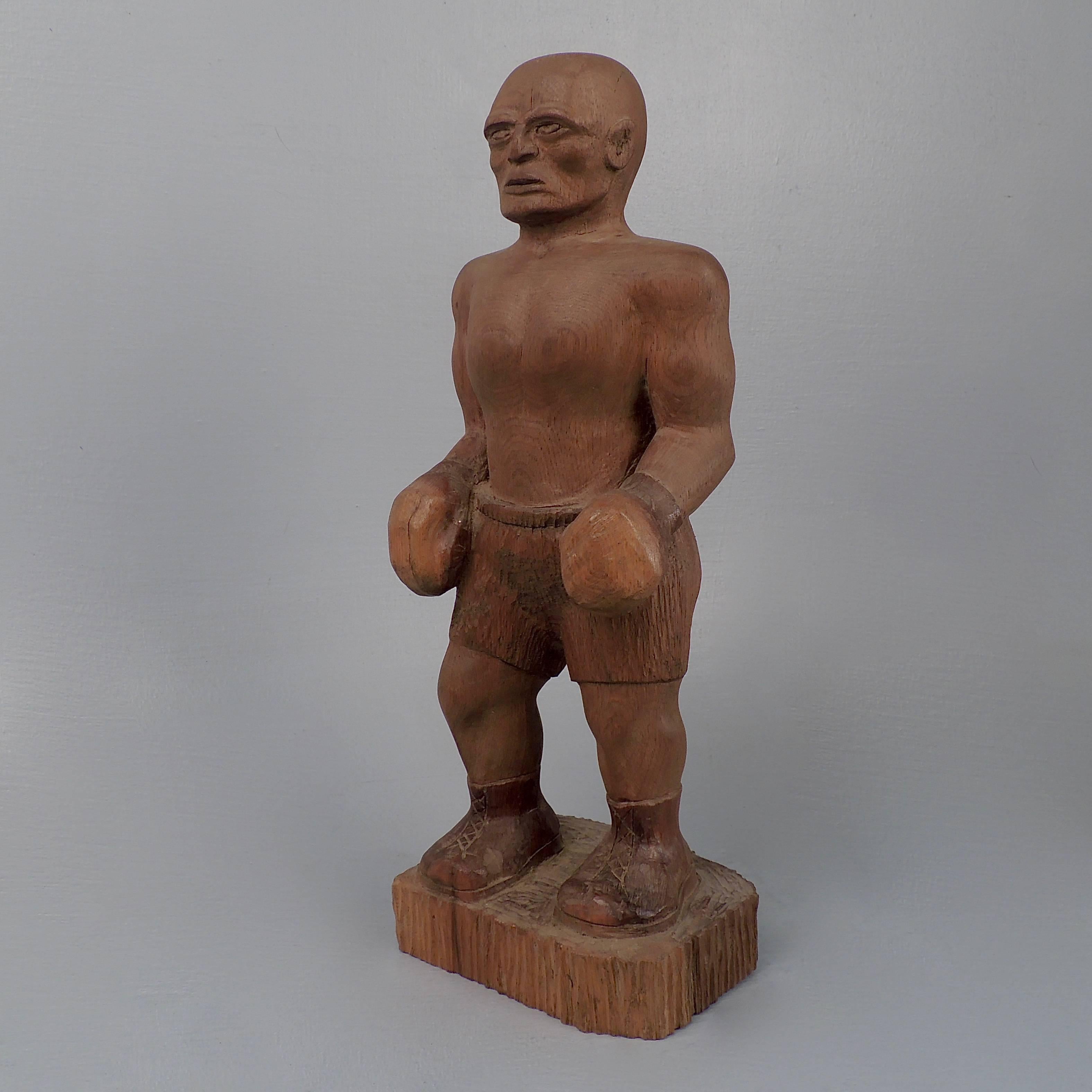 A terrific 20th century carved wooden folk art sculpture of a boxer. The boxer stands erect, one foot slightly behind the other, with his hands at his side. He has a slightly flattened nose and slightly oversized ear. A depiction of Jim Thorpe
