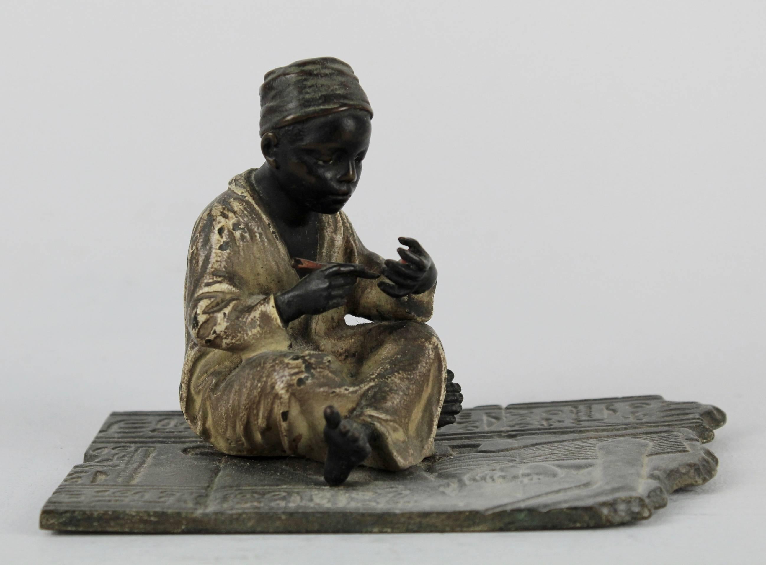 A fine early example of a signed F Bergmann cold painted Orientalist bronze. It depicts a seated Arab or North African youth with pen in hand. He sits with legs crossed on a floor that has low relief hieroglyphics and is a student or scribe. The boy