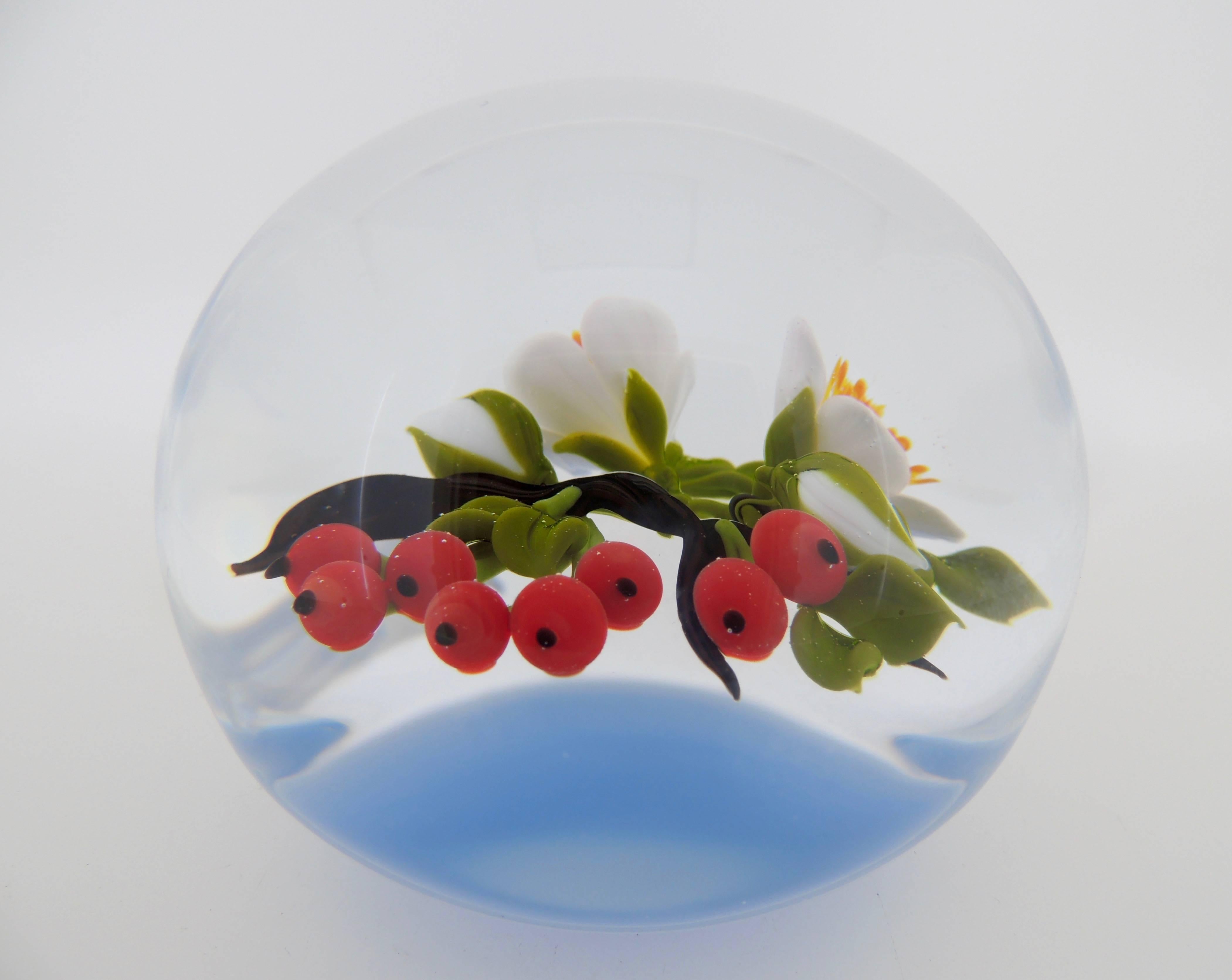 A fine example of one Victor Trabucco's large scale paperweights. The lampwork includes a branch with red berries and flower blossoms suspended above a milky-blue colored ground. 

There is a 