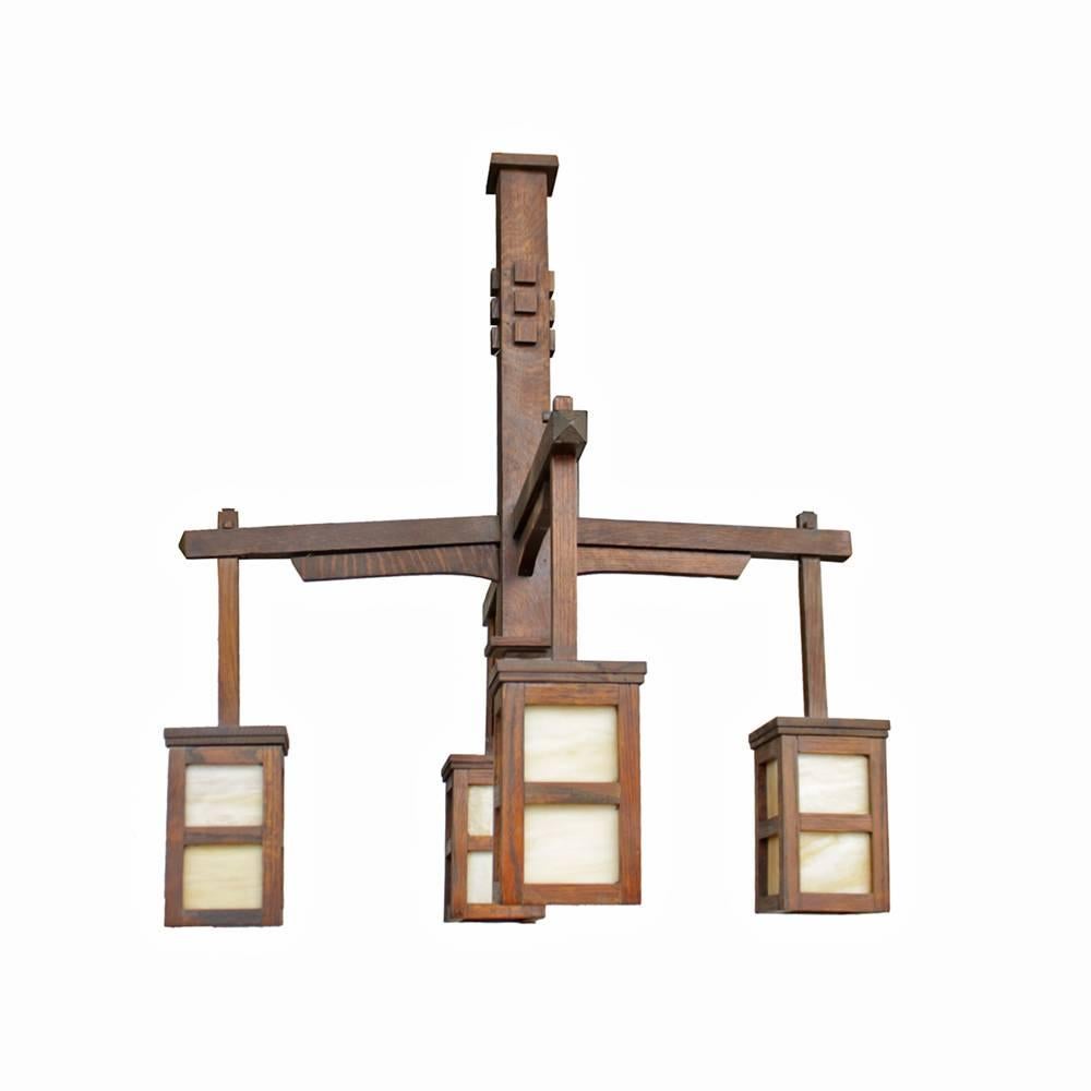 Classic lines and details in this absolutely paragon arts and crafts era chandelier. Evoking the Craftsman style almost immediately with its geometric Silhouette, this four-armed lantern type light fixture features solid oak construction and slag